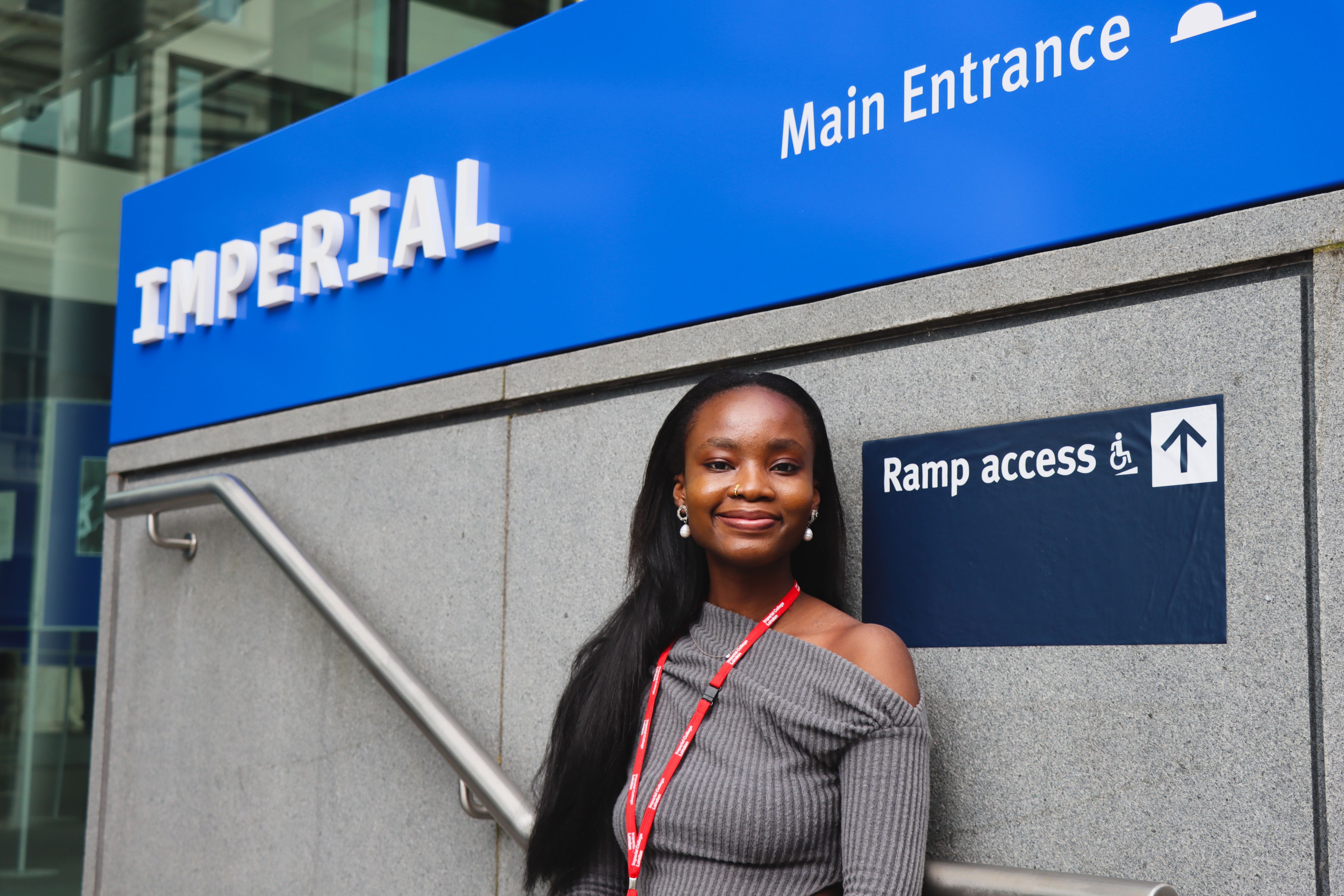 Ifeoluwa standing in front of the Imperial logo on the steps at the main entrance to Imperial's South Kensington campus