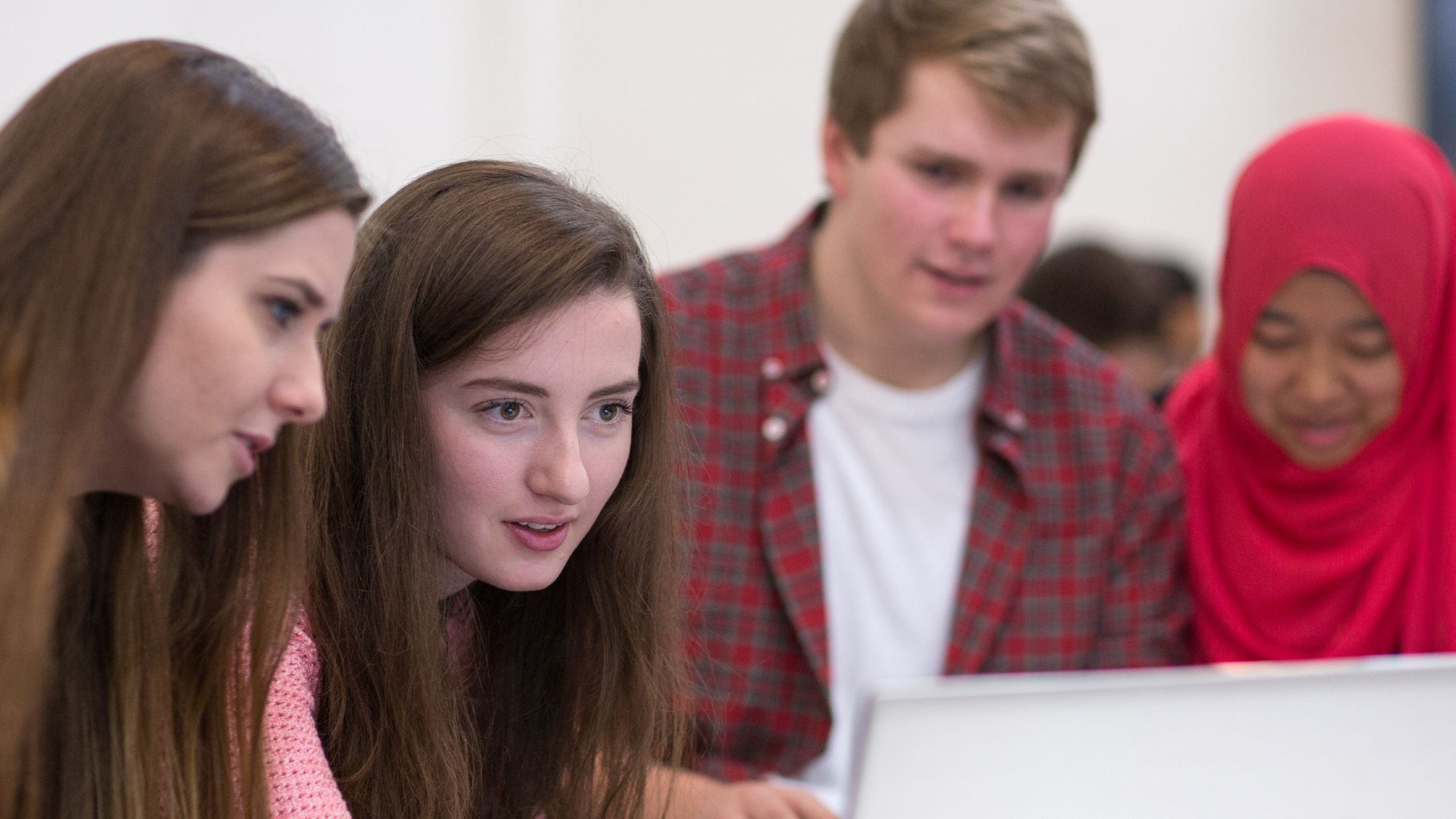 Students smiling while gathered around a laptop.