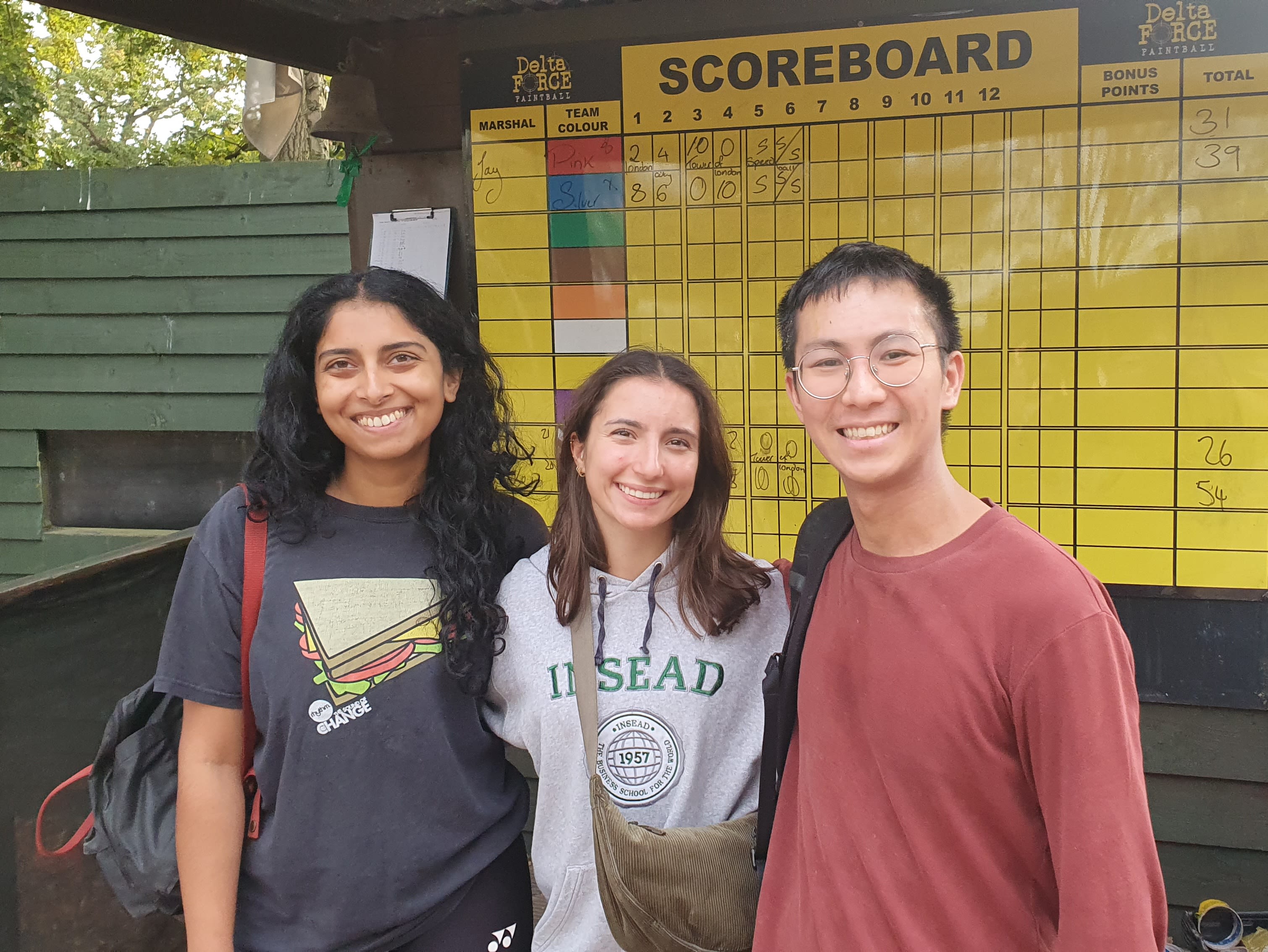 JJ with two friends standing in front of a scoreboard for 'Delta Force Paintball'