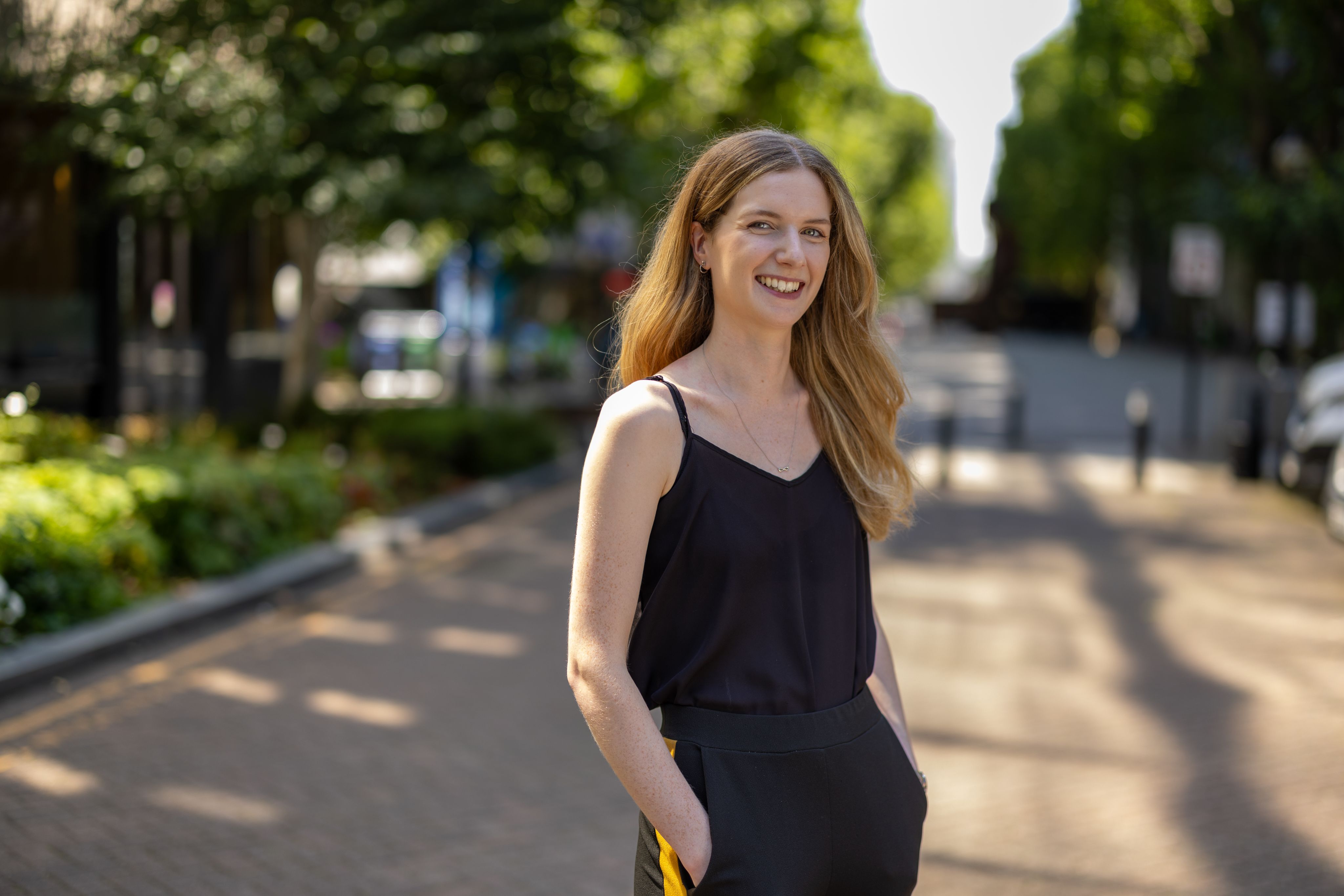Katie on South Kensington campus, with green trees in the background
