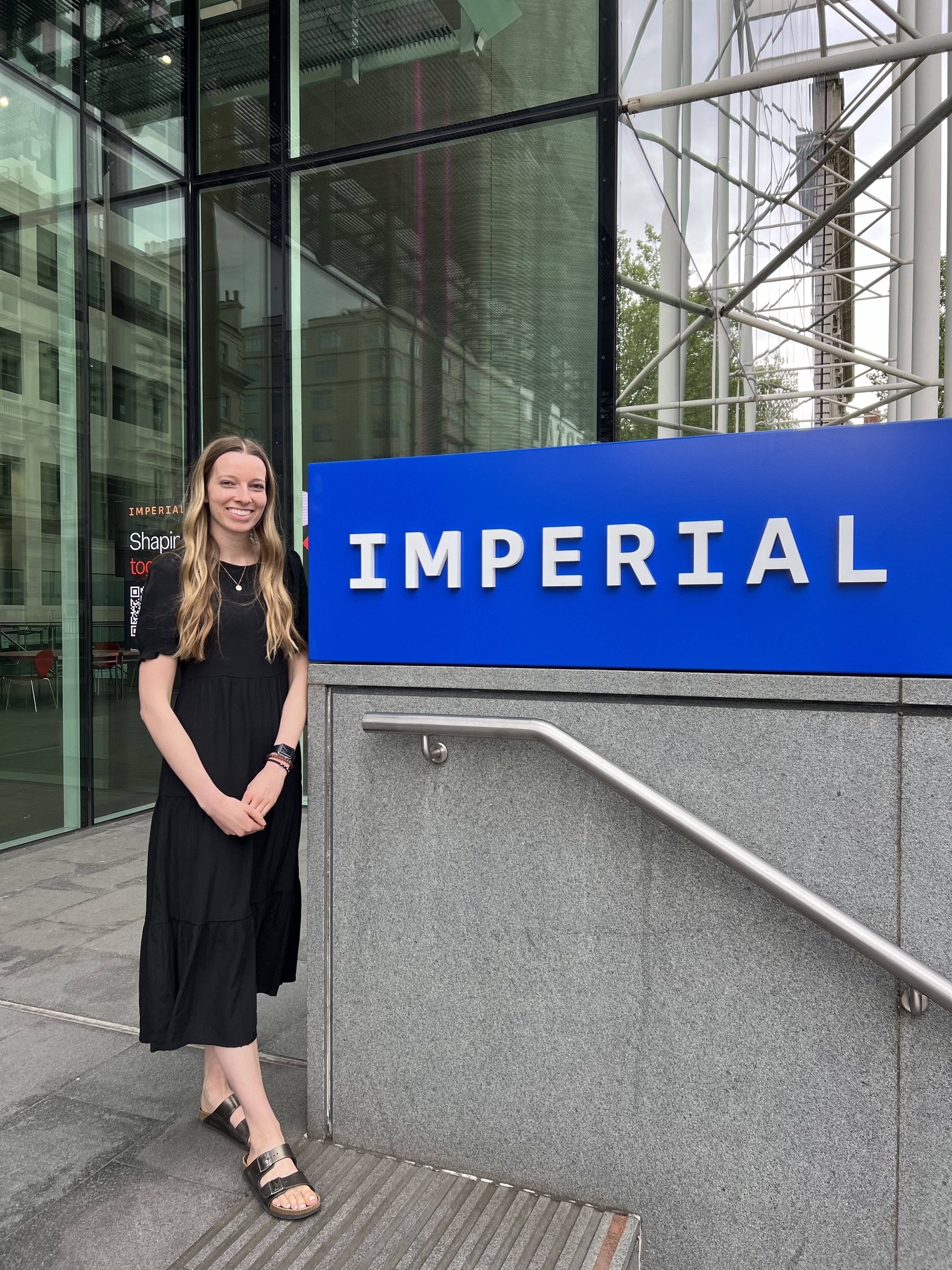 McKenna standing next to the Imperial logo by the stairs leading to South Kensington Campus main entrance