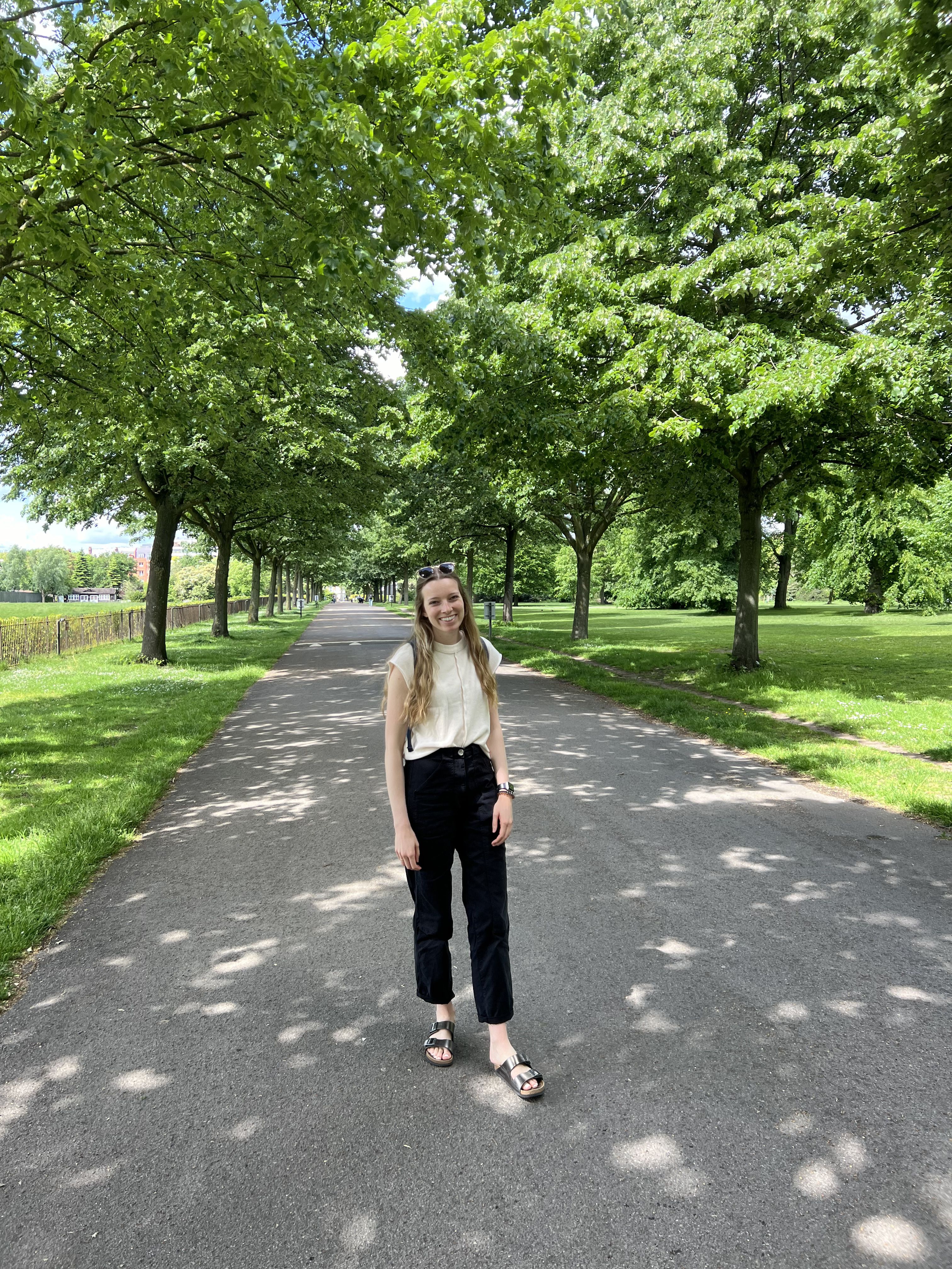 McKenna standing in Kensington Gardens with a line of green trees behind her