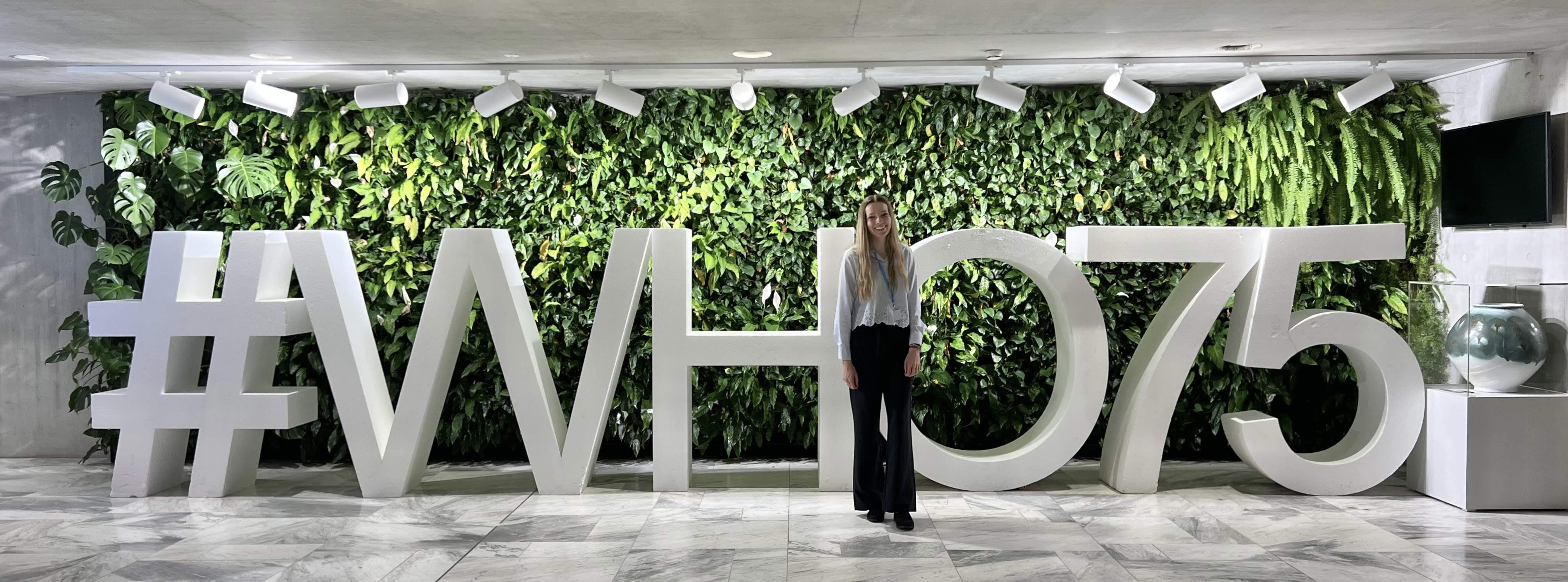 McKenna standing in front of big standing letters spelling #WHO75