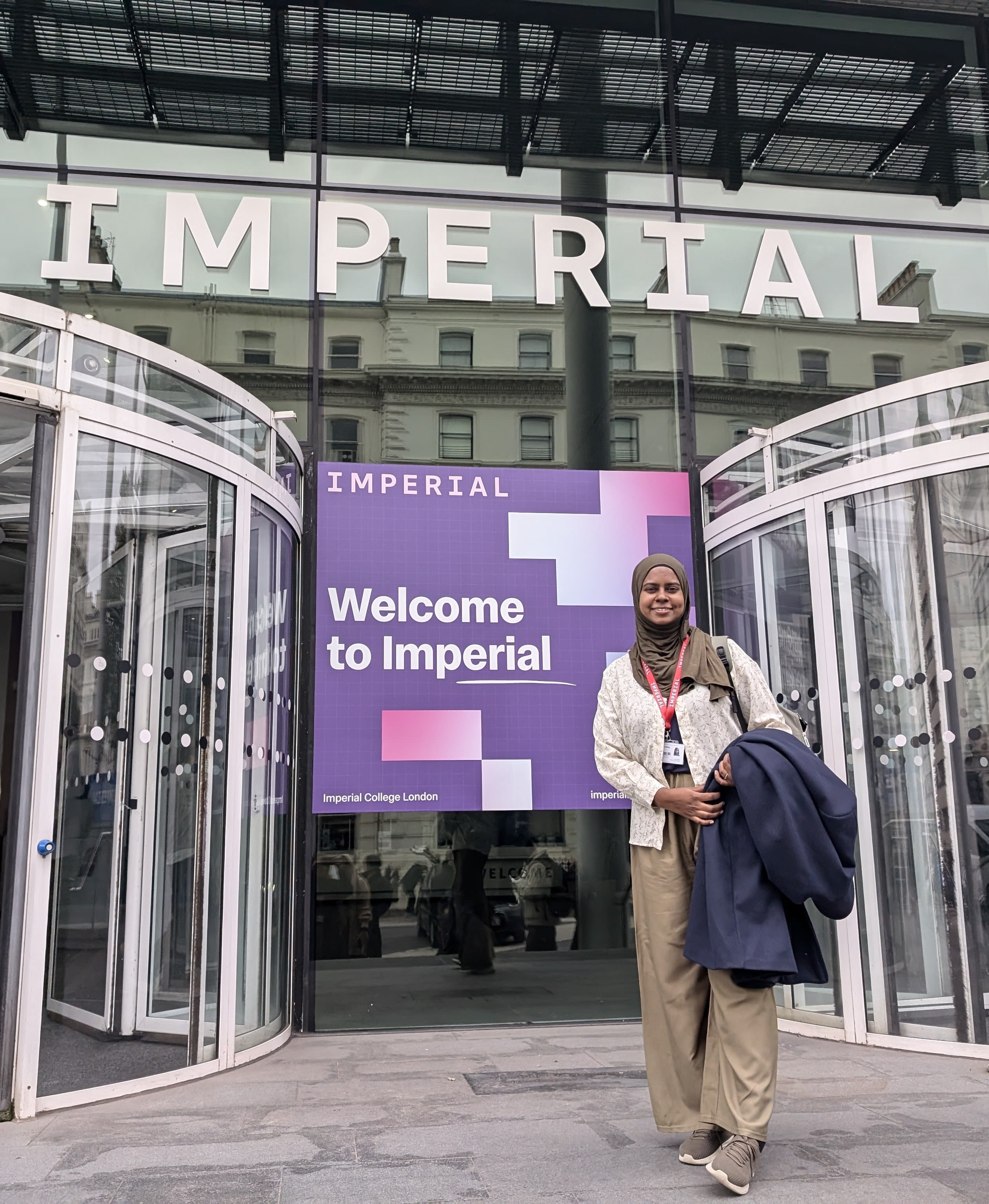 Nafisah standing by a sign saying 'Welcome to Imperial' at the main entrance to South Kensington Campus
