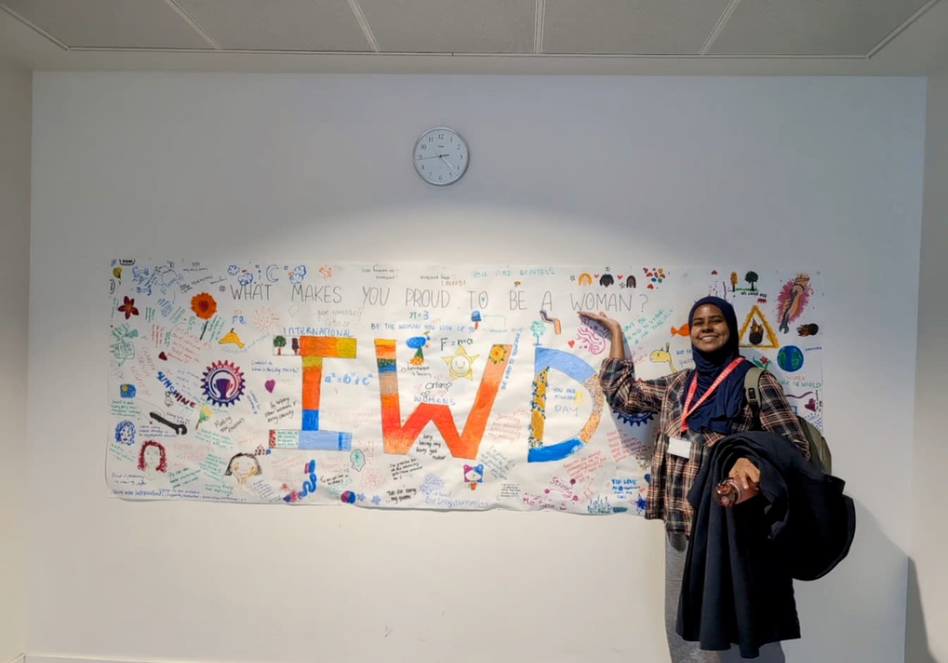Nafisah standing next to her addition to an International Women's Day poster on the wall