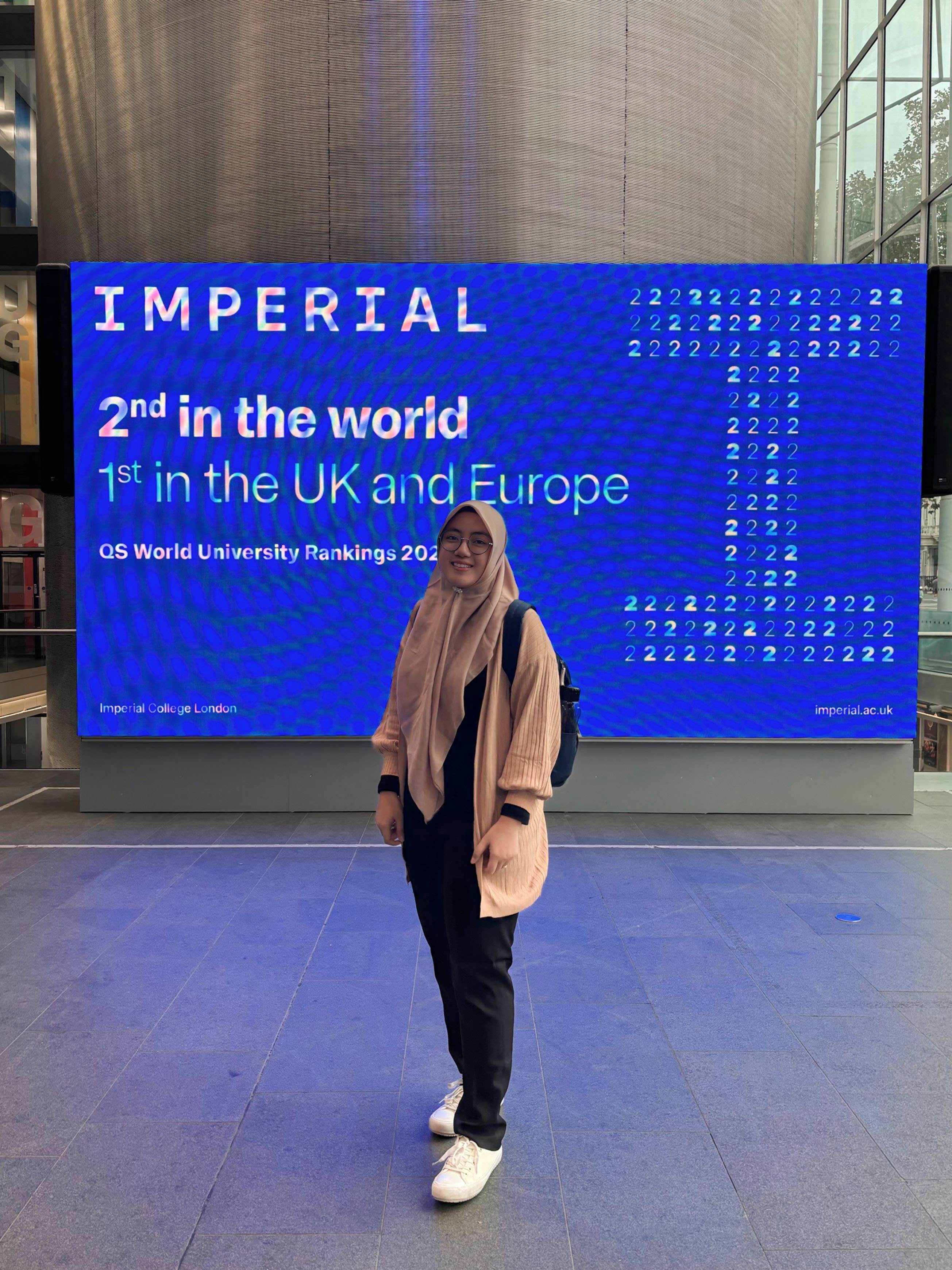 Nava standing in front of a screen with the Imperial logo and text that says "2nd in the world, 1st in the UK and Europe"