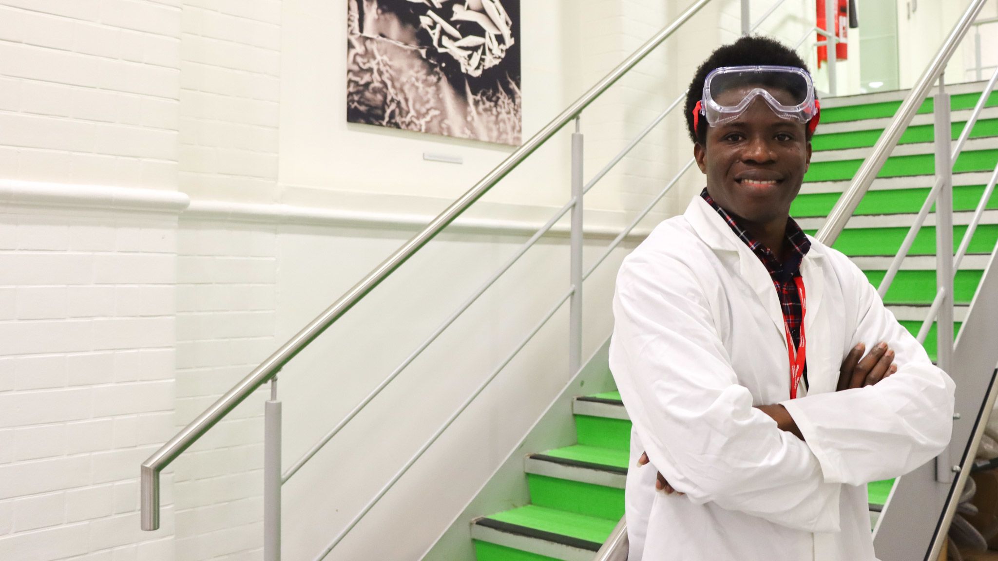 Oluwafemi smiling at the camera, wearing PPE including a lab coat and safety googles