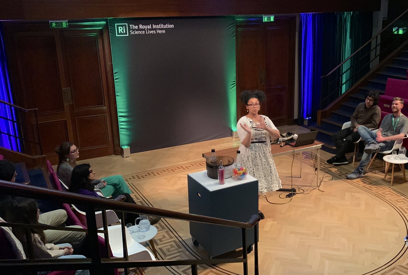 Vanessa standing in the middle of a lecture theatre, giving a talk at the Royal Institution