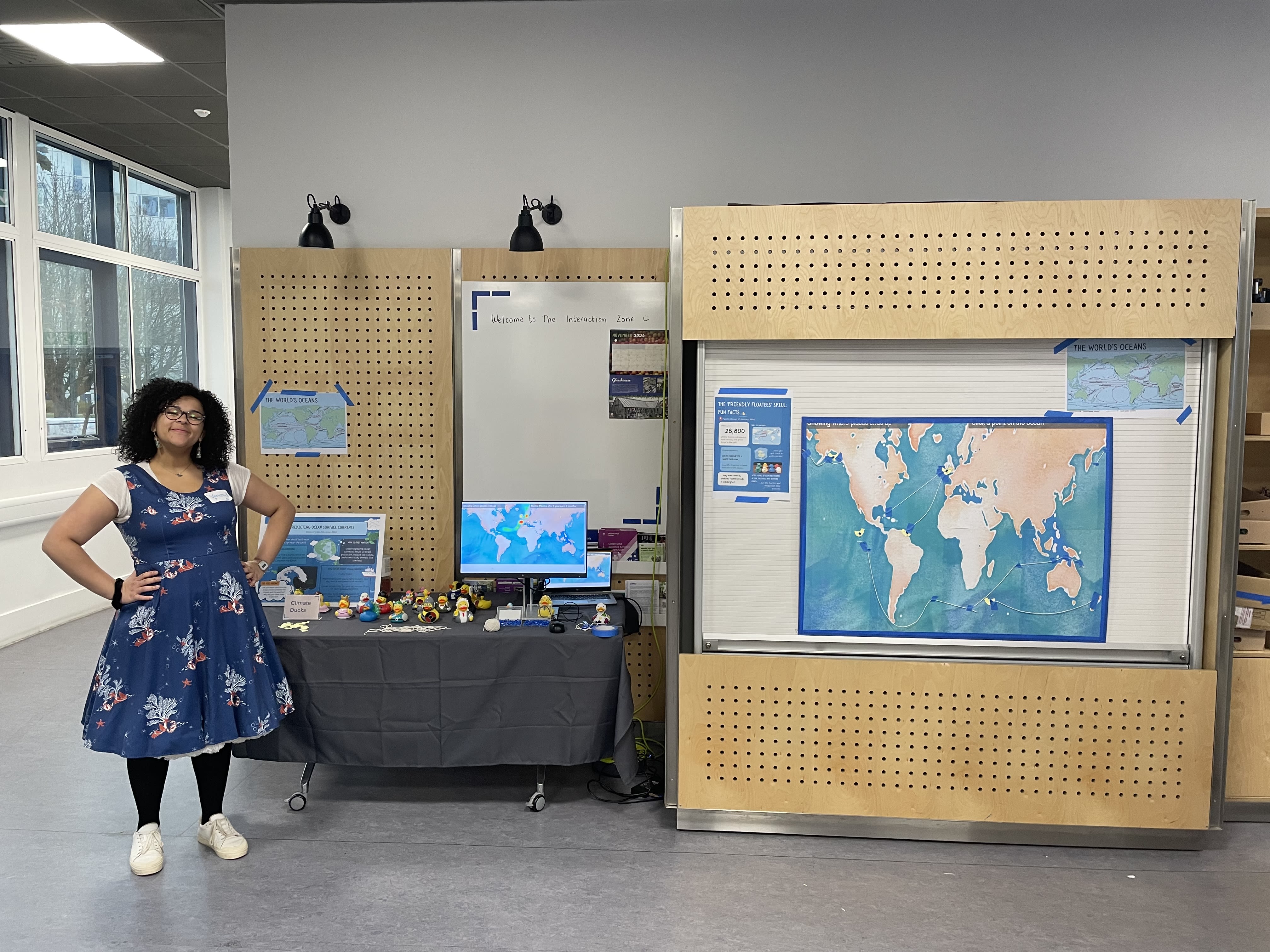 Vanessa standing in front of her project showcase including world maps in the Invention Rooms on White City Campus