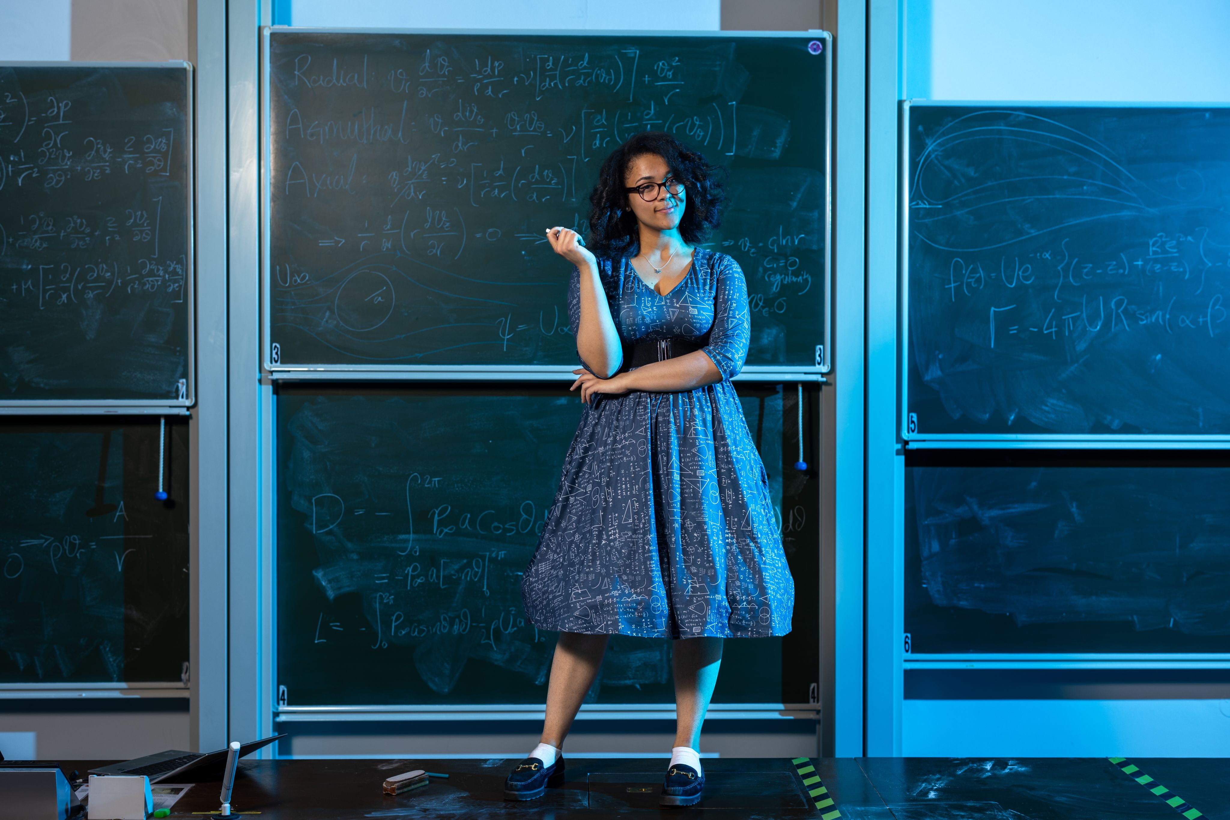 Vanessa holding some chalk and standing in front of a blackboard with maths equations on it