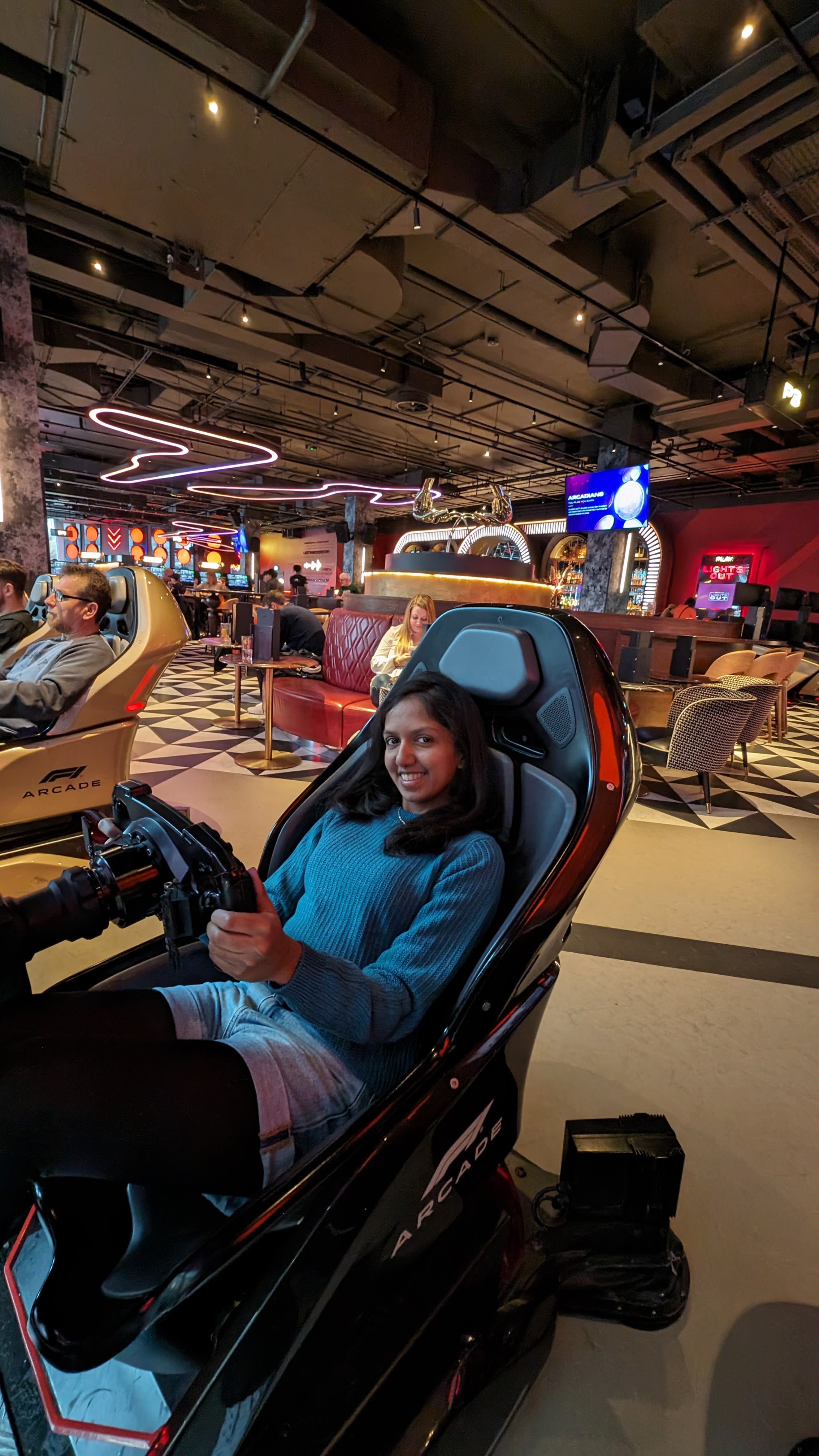 Vanya sitting in a car racing game chair at an arcade