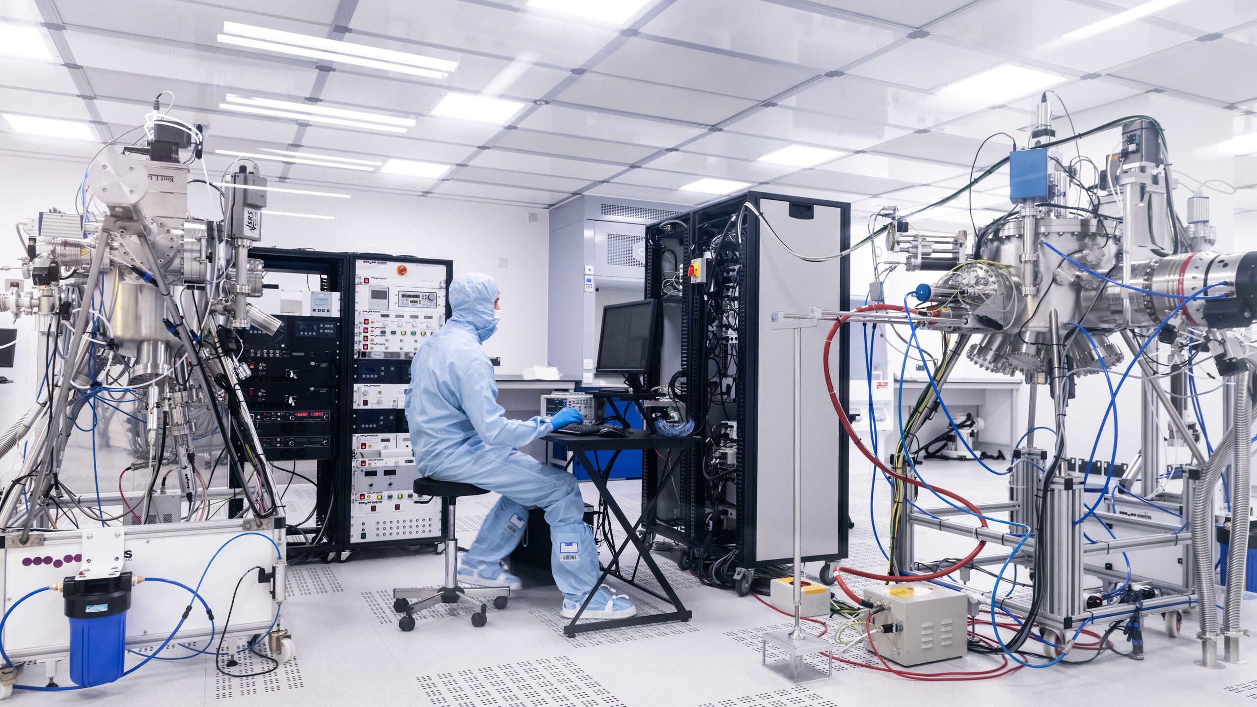 A researchers in a plastic coverall operates a scientific instrument in a clean room.