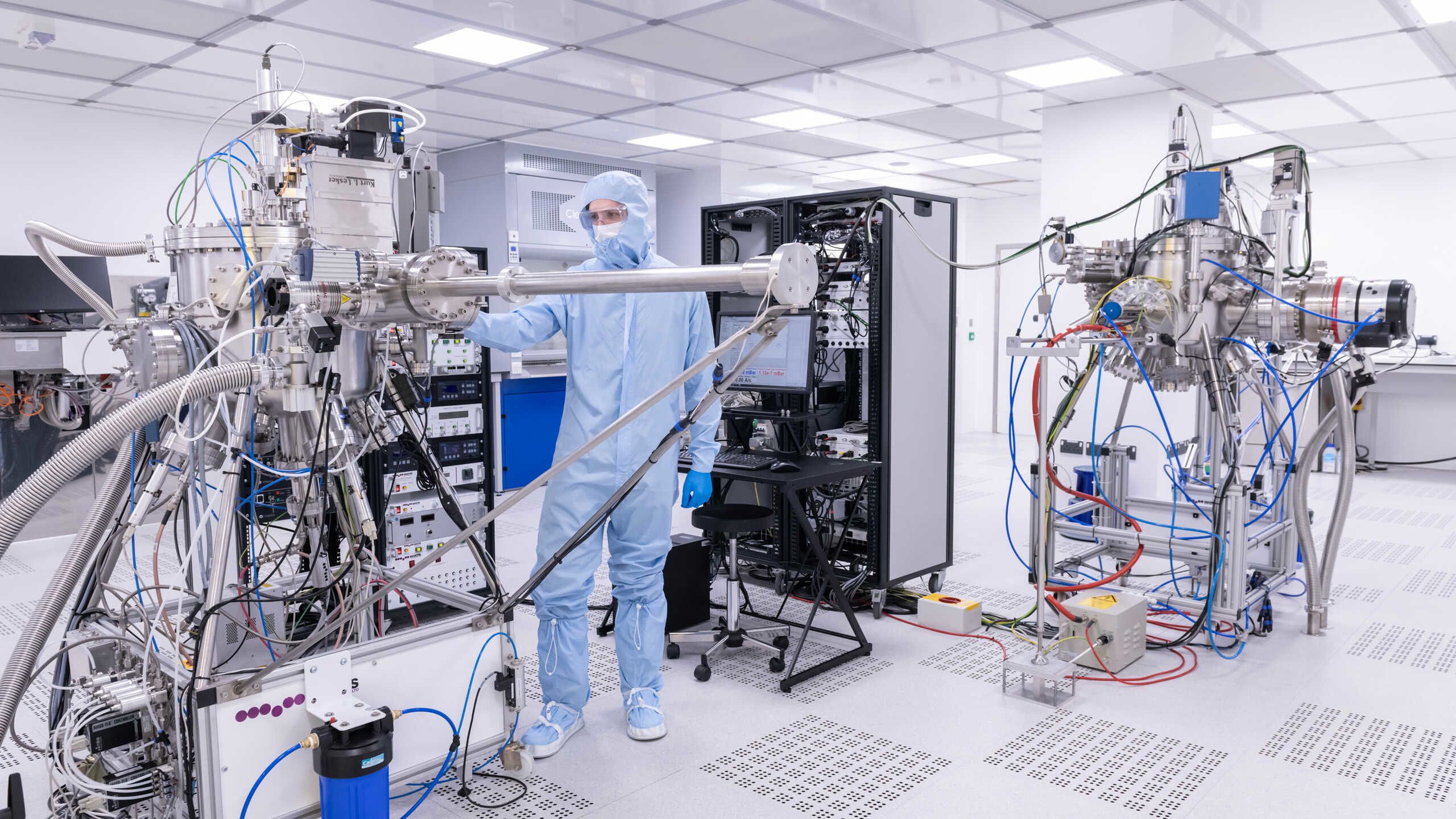 A researchers in a blue plastic coverall operates a scientific insturment in a clean room.