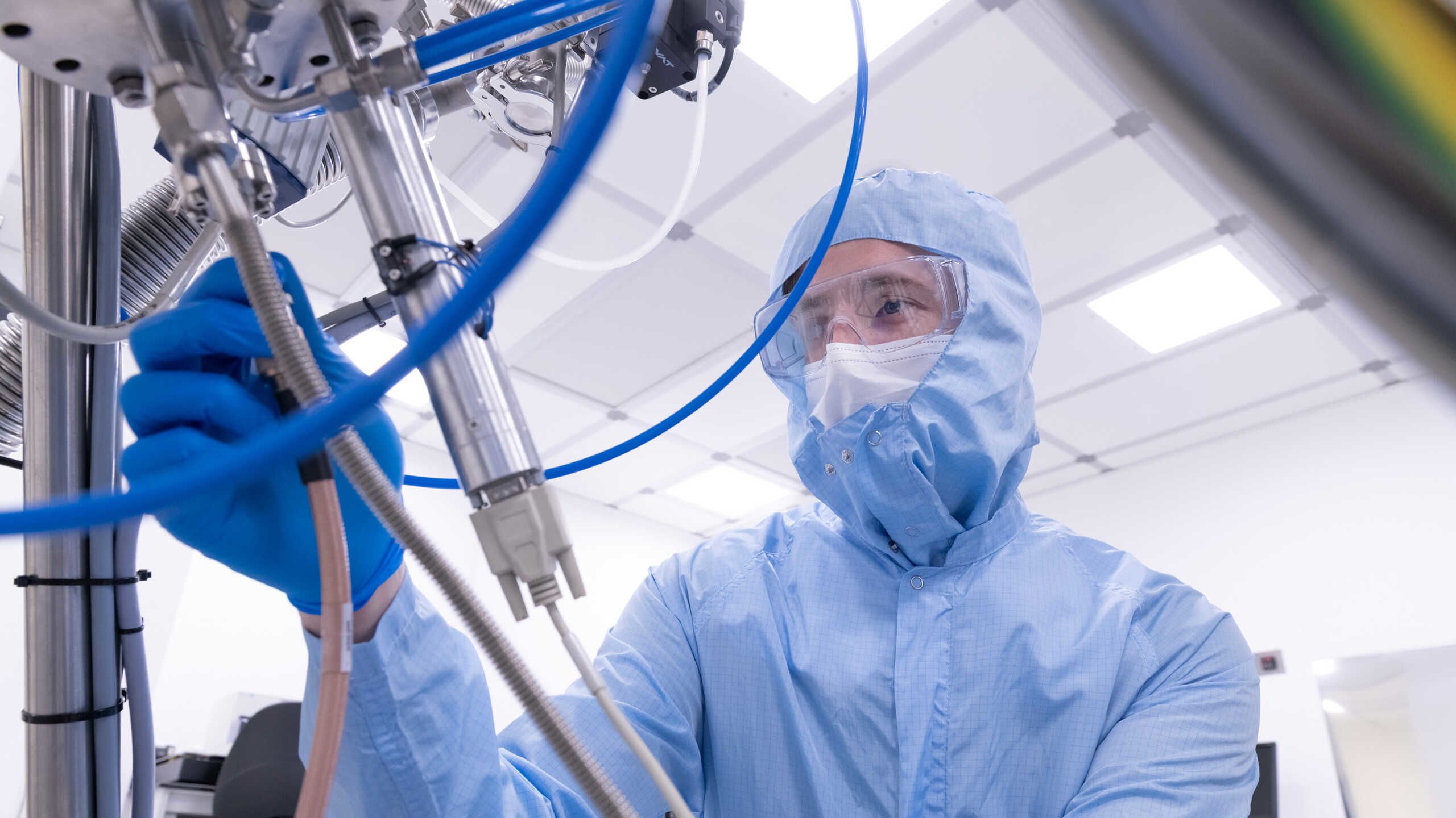 A researcher in a blue coverall and safety glasses adjusts a scientific instrument.