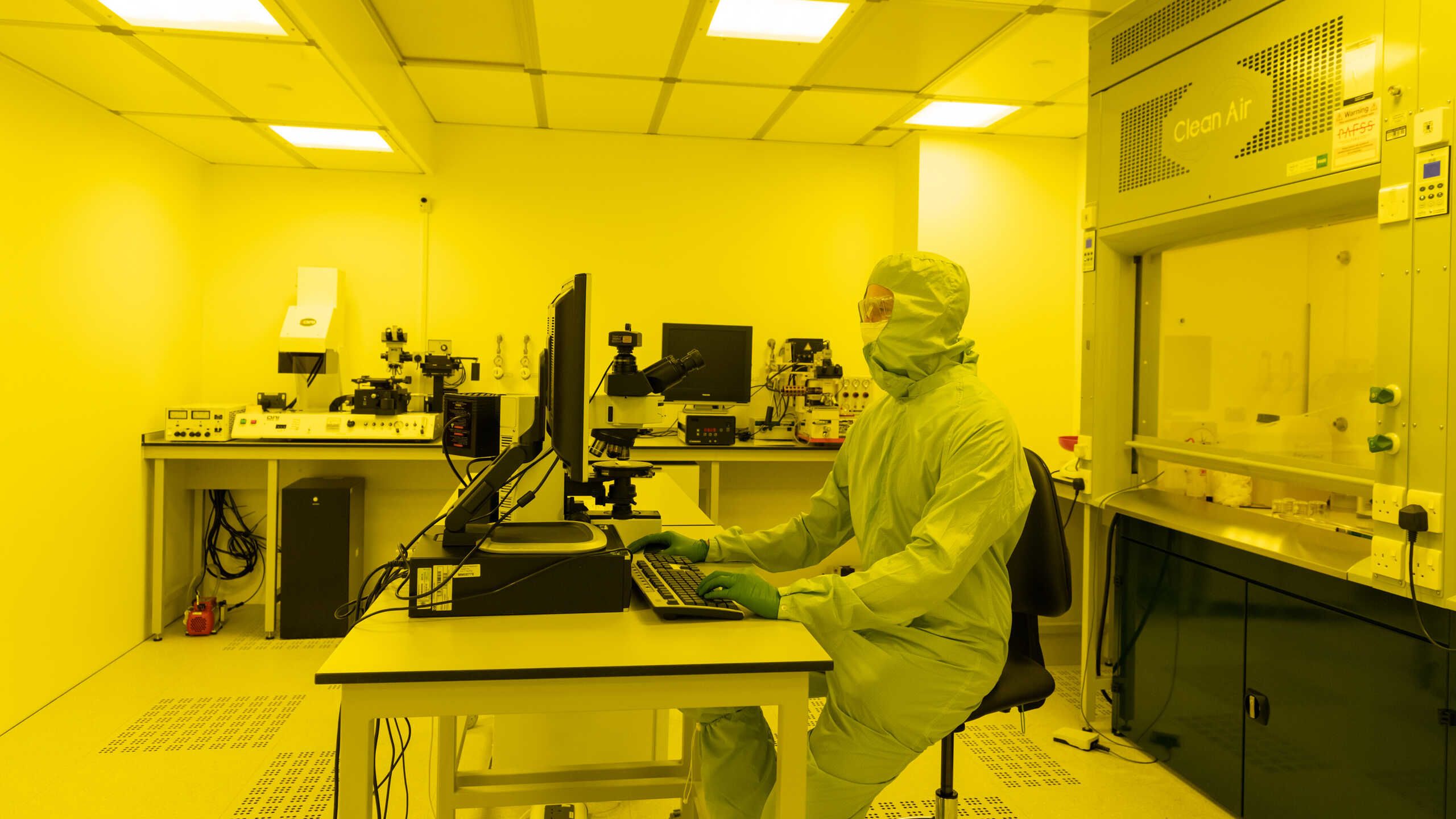 A researcher in a plastic coverall works in a laboratory bathed in yellow light.