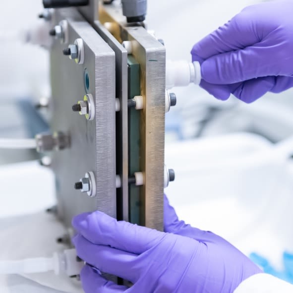 Hands in purple plastic gloves hold a block made of metal plates.