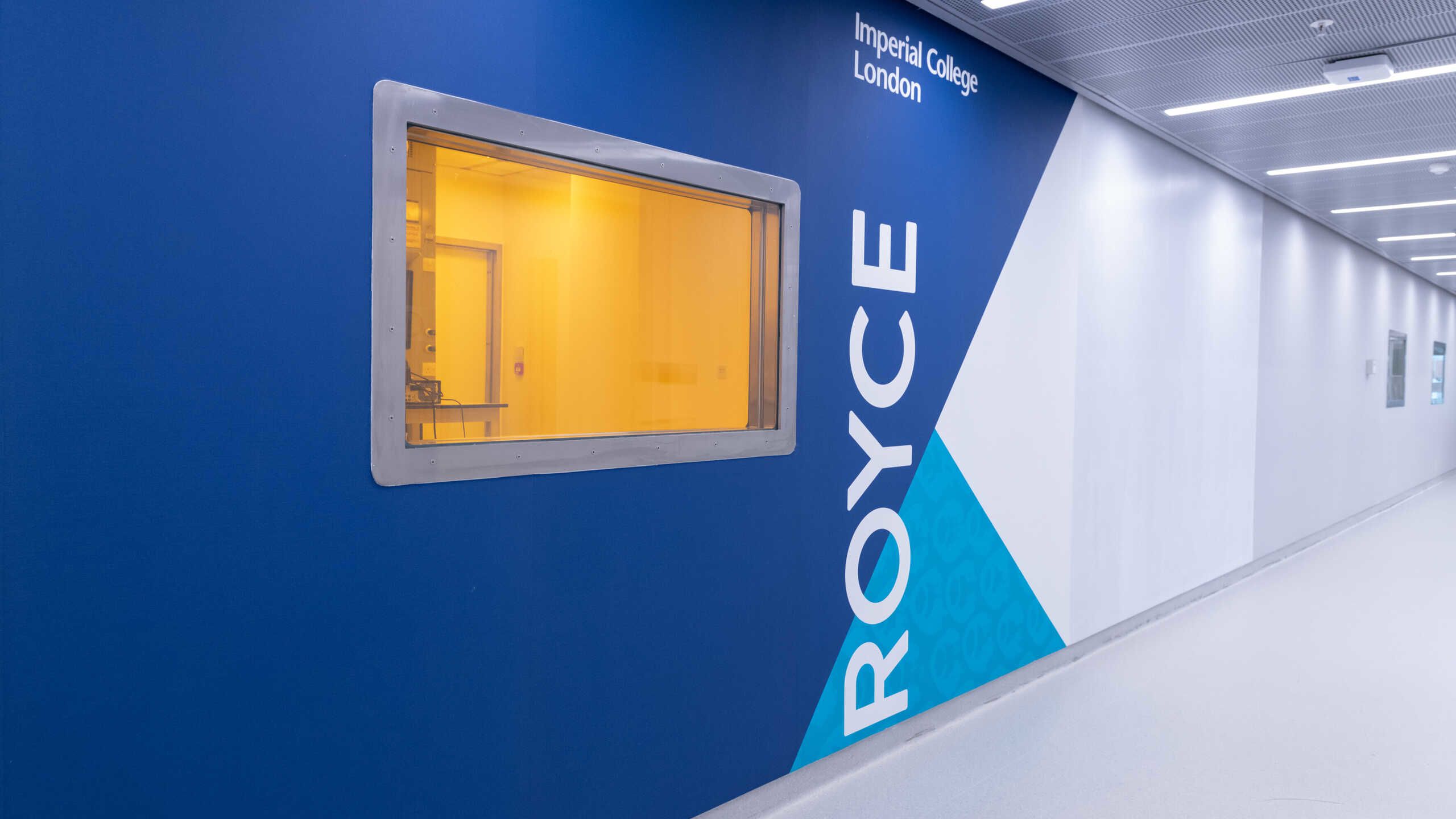 A window let into a corridor shows a yellow light. The name Royce on the wall.