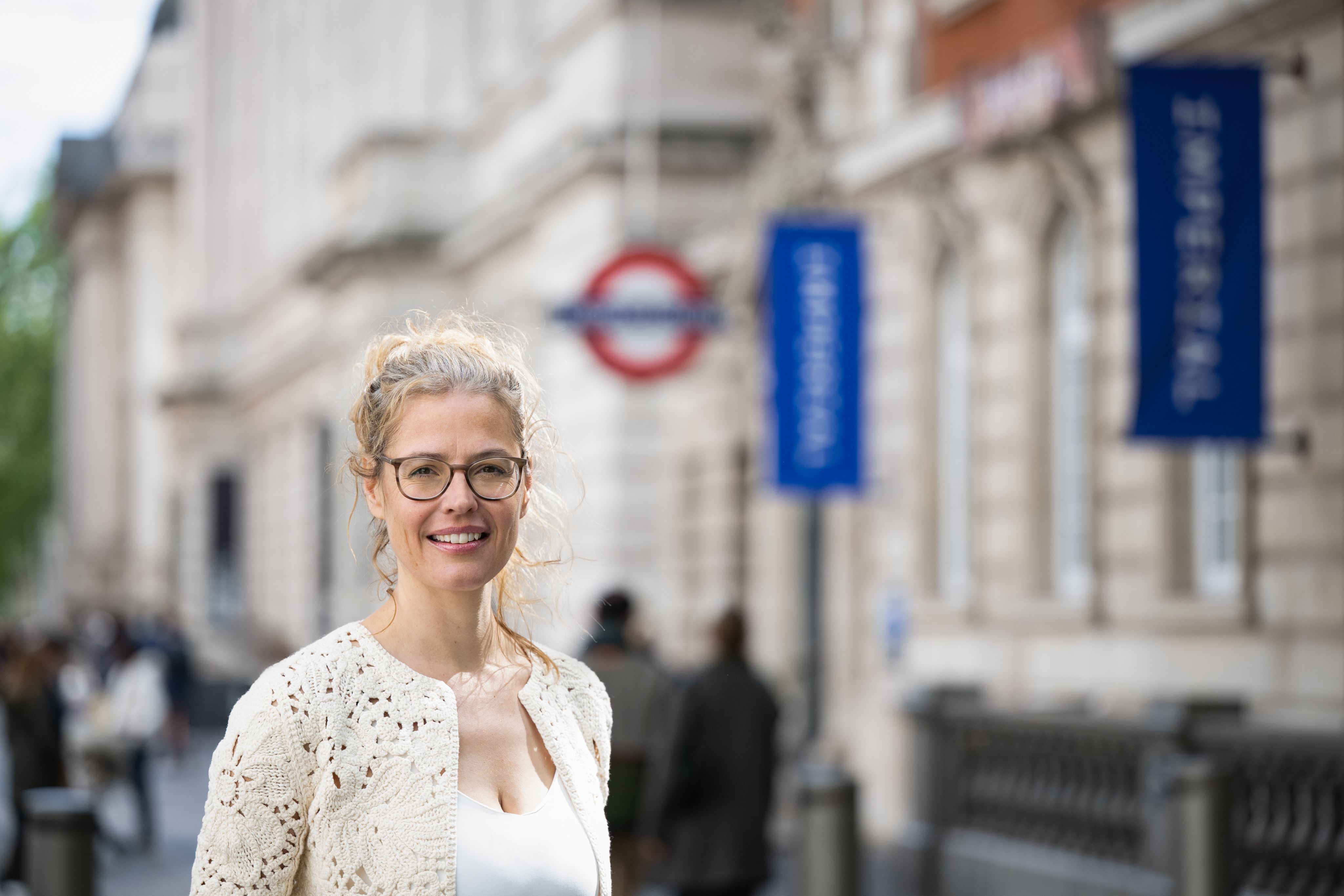 Close up of Sabine in front of a tube station with Imperial flags in the background.