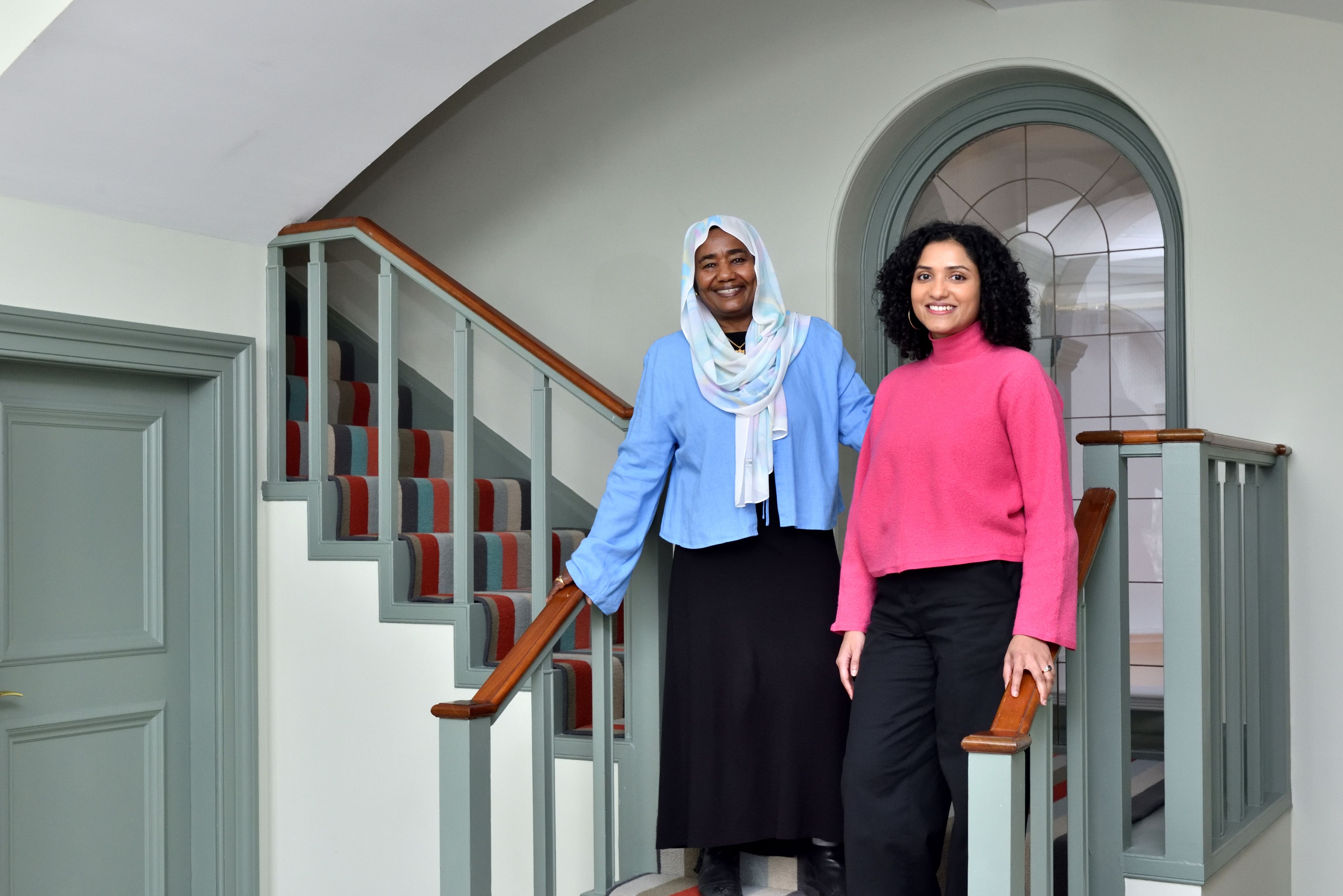 Sarindi Aryasinghe and her community partner, Phayza Fudlalla, standing side-by-side together on a staircase smiling at the camera.