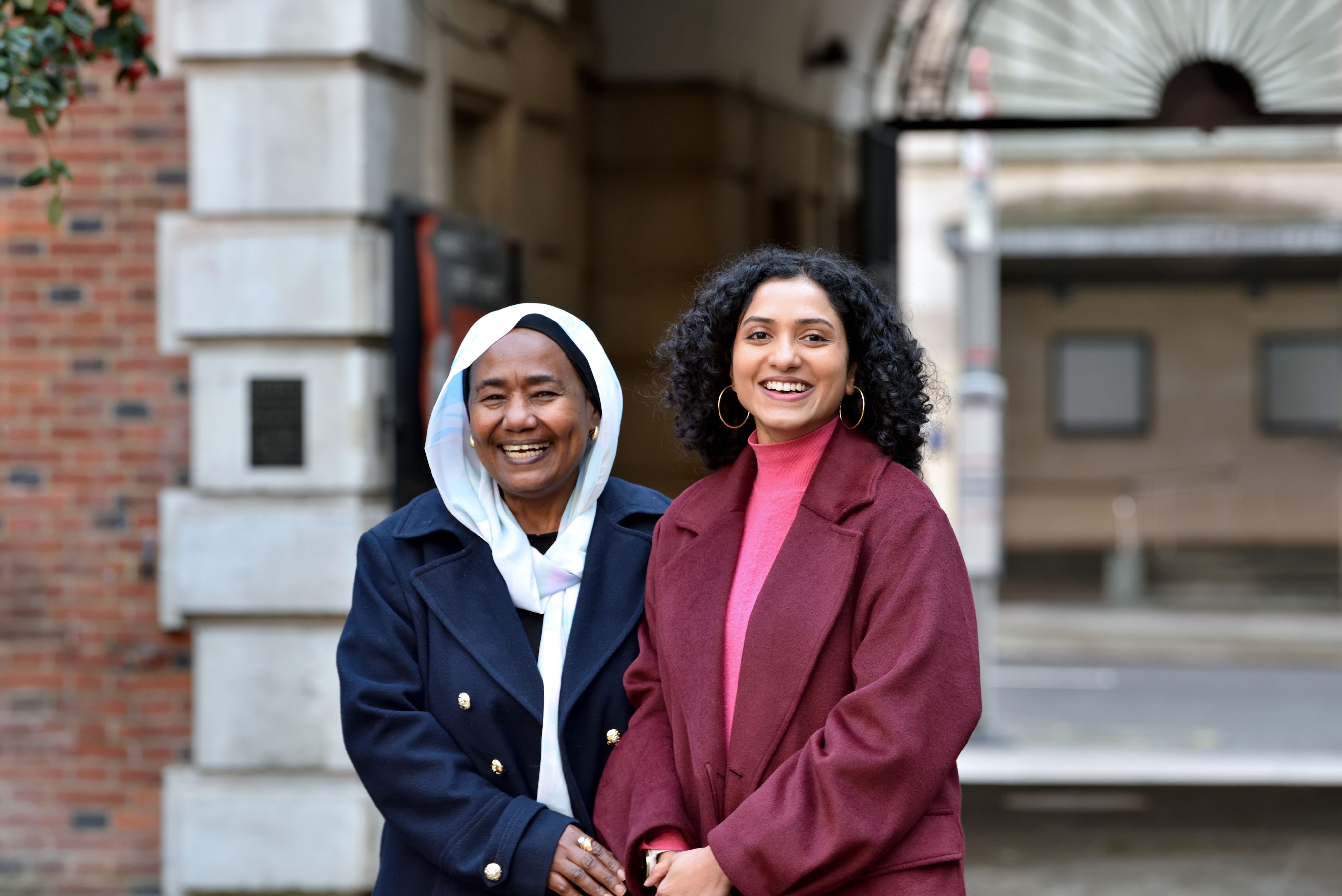 Sarindi Aryasinghe and her community partner, Phayza Fudlalla, standing shoulder-to-shoulder outside laughing towards the camera. 