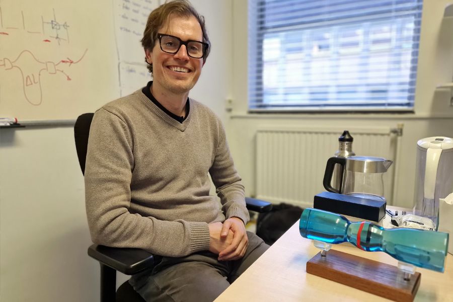 A scientist sits at a desk in the Department of Physics. There is a model of an optical fibre on the desk