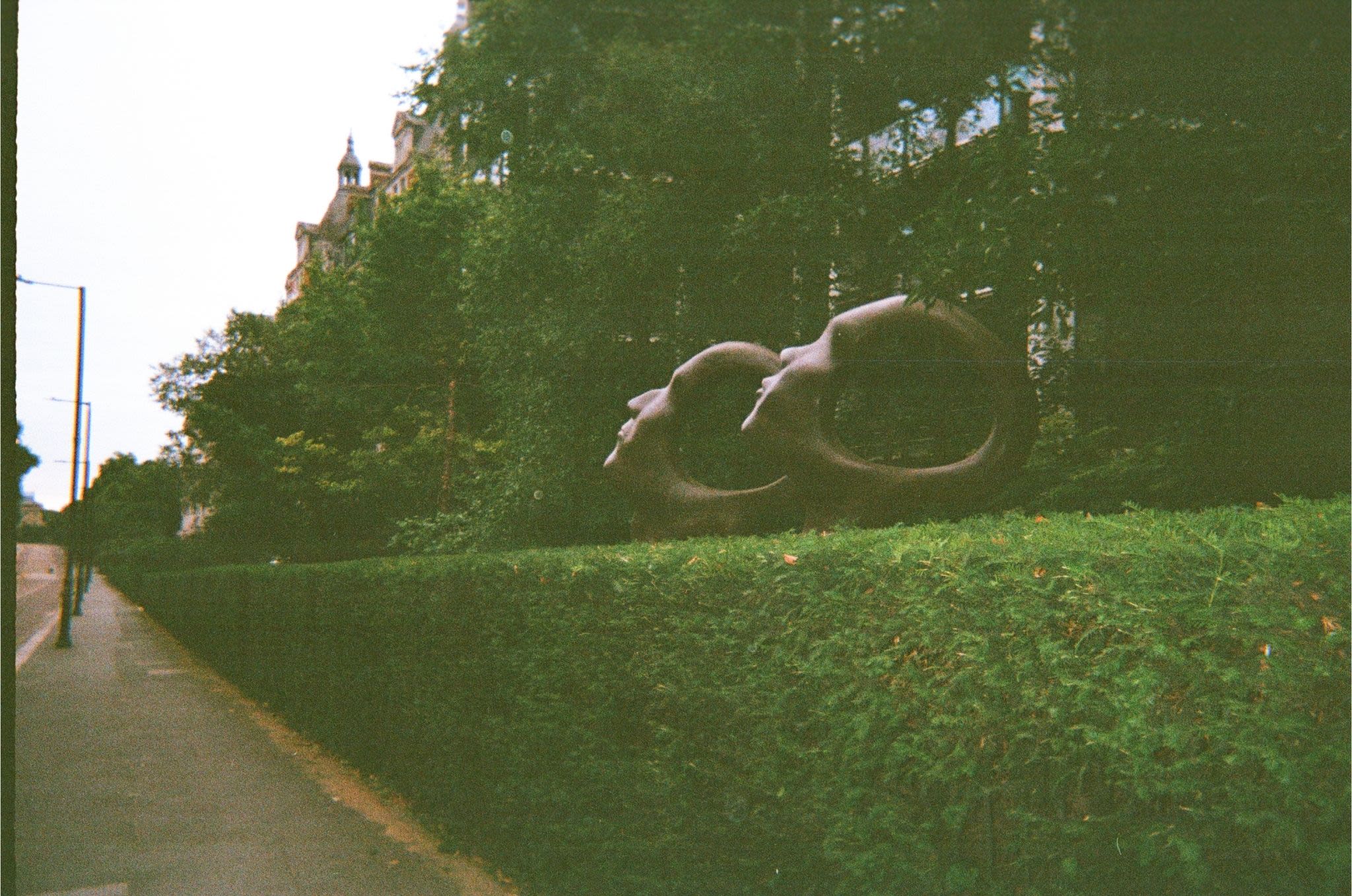 Two metal statues beside the pavement. The statues depict heads with holes in the middle.