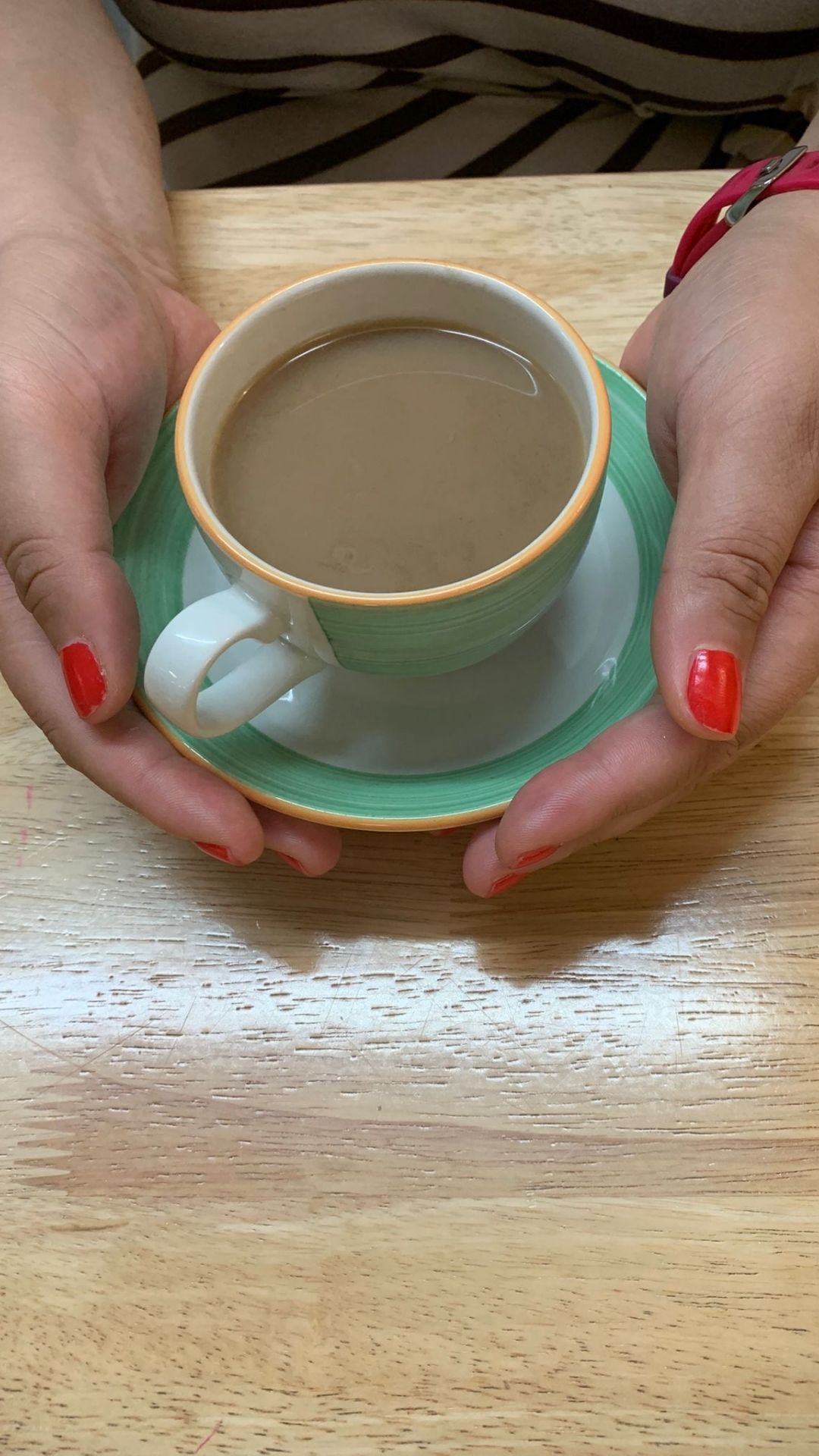 Two hands holding a green mug filled with tea.