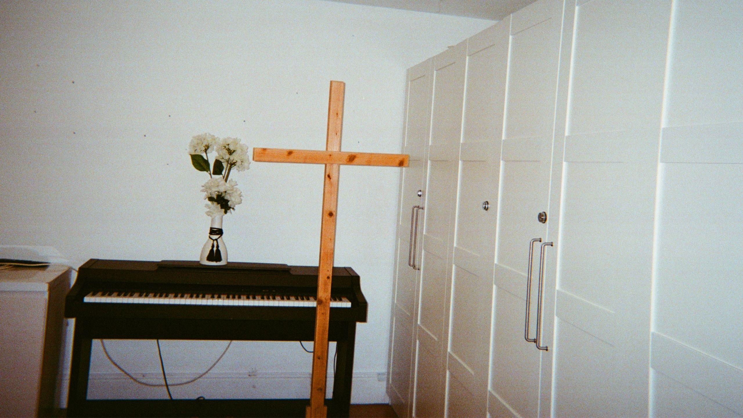 A piano with a vase of flowers on top of it and a wooden cross in front of it.
