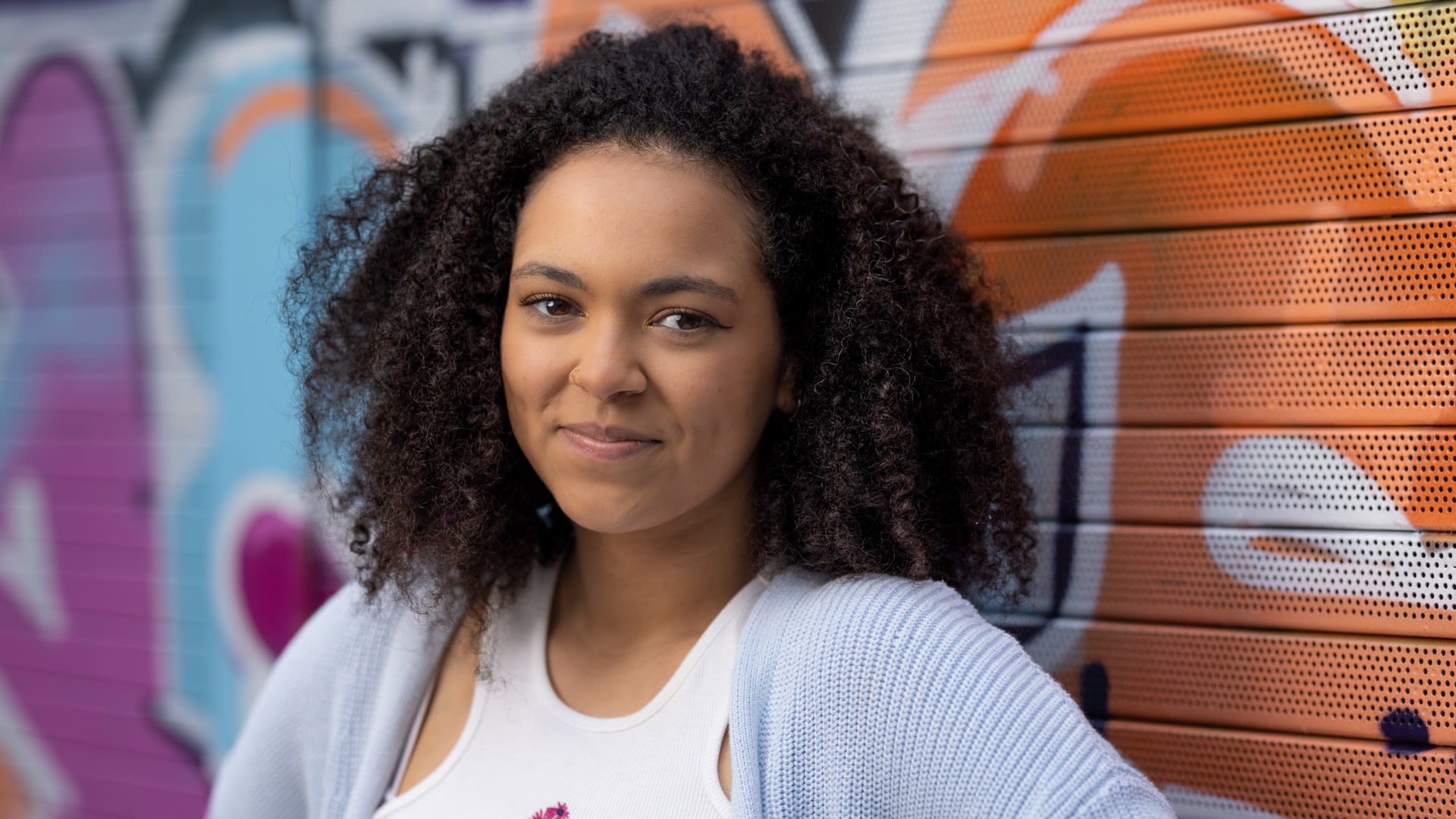 Hollie smiling at the camera against a bright graffiti wall 