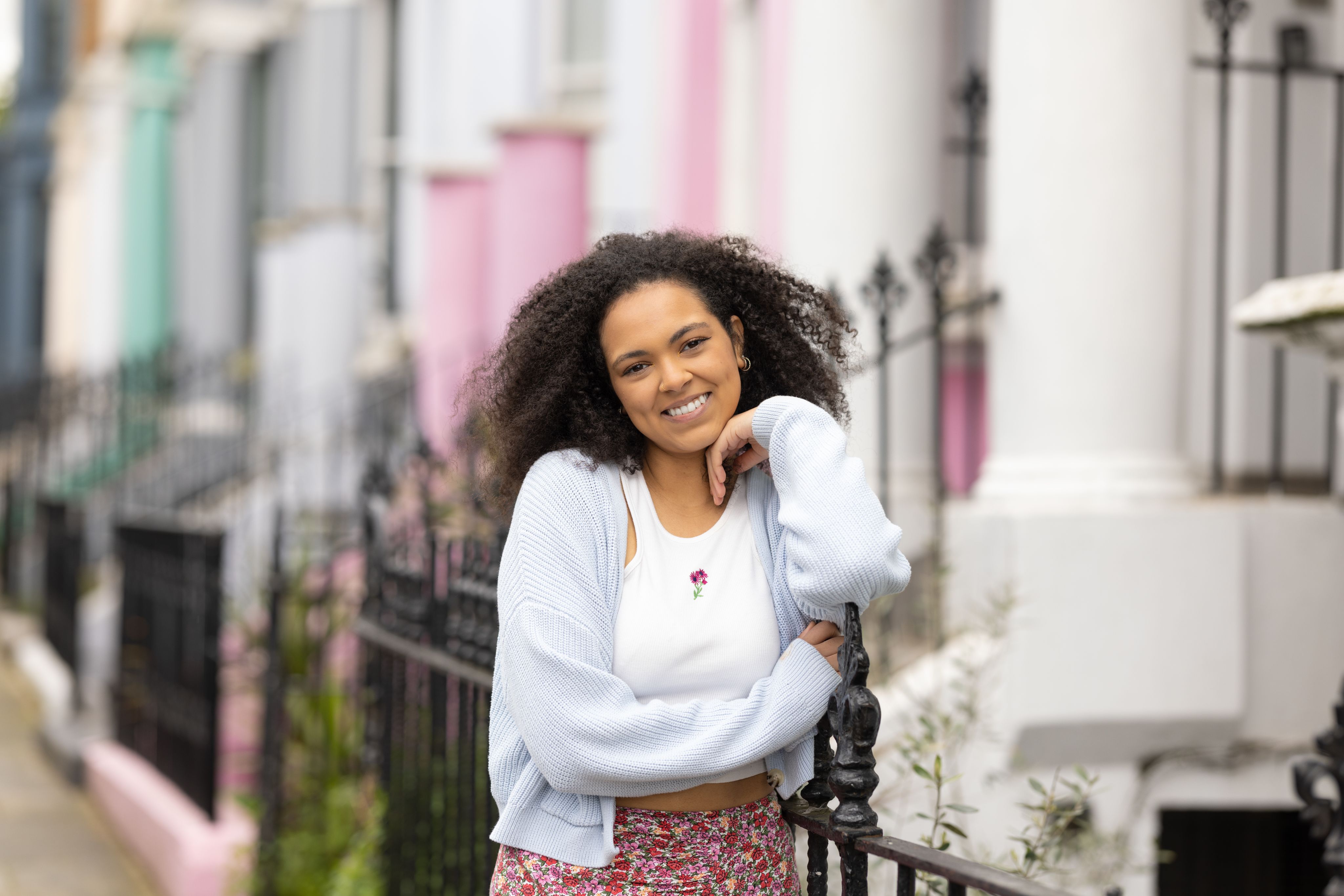 Hollie leant against railings on a colourful street