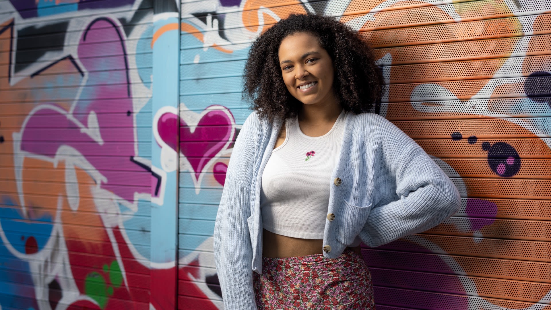 Hollie smiling at the camera against a colourful graffiti wall