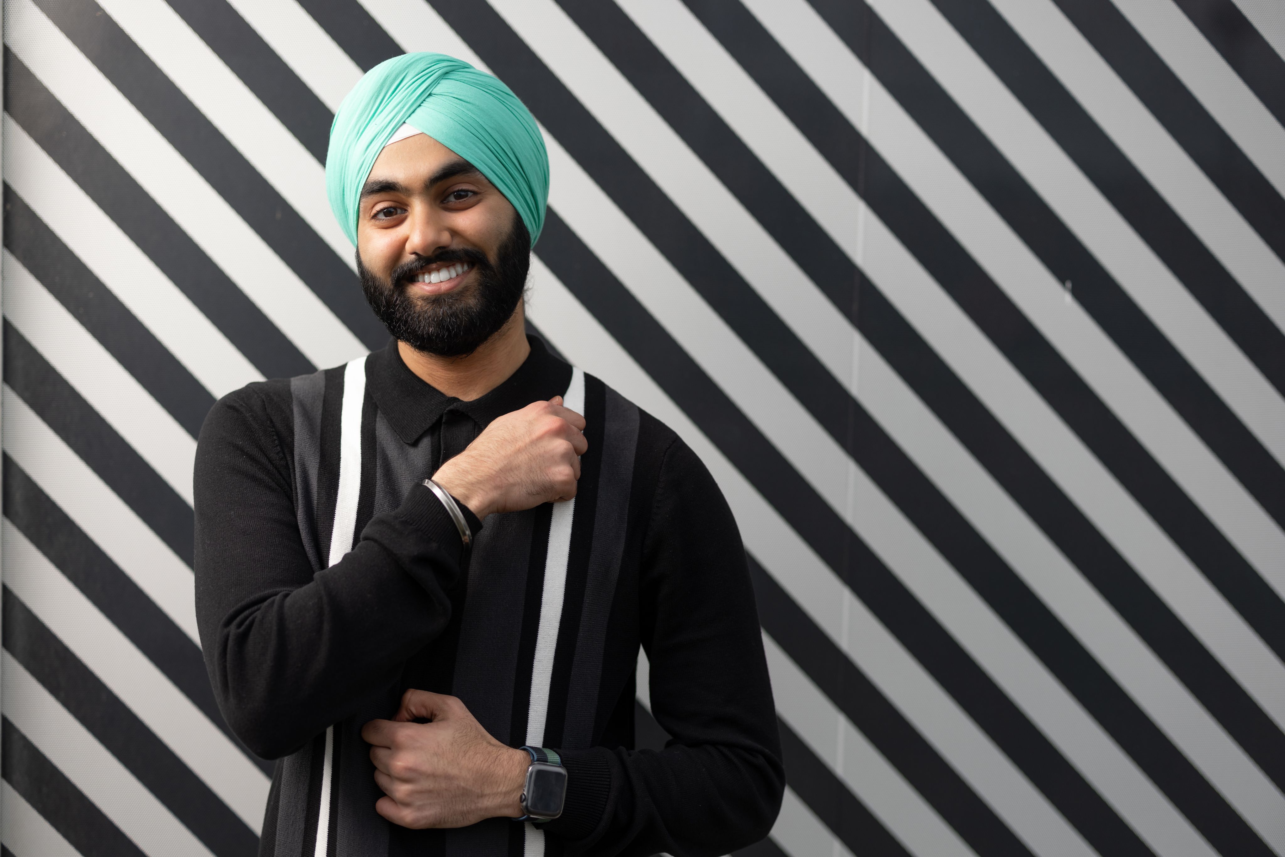 Juproop smiling at the camera against black and white striped background