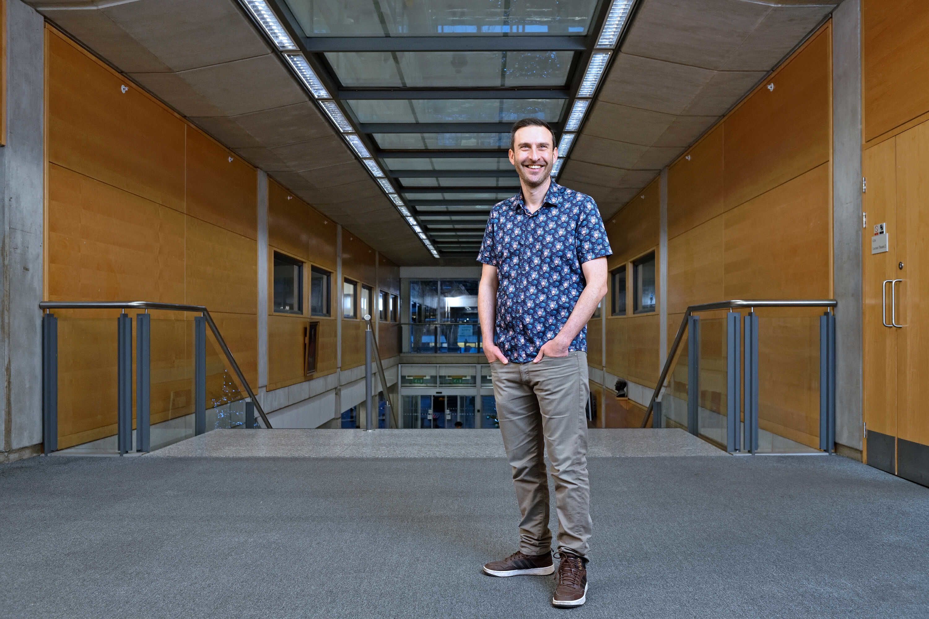 Simon stood smiling into the distance at the top of the stair case in the Sir Alexander Flemming building.