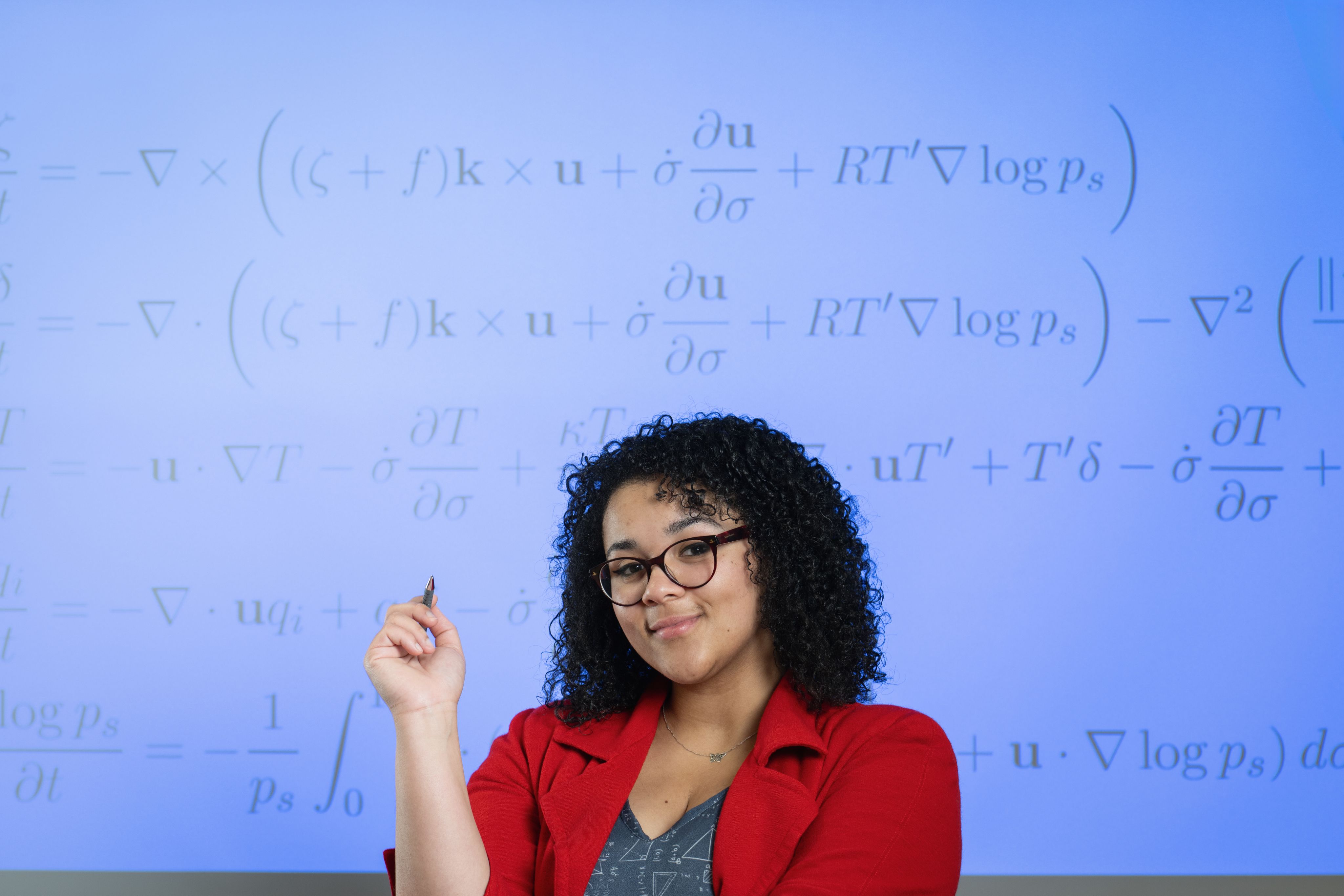 Vanessa smiling in front of a screen with maths equations.