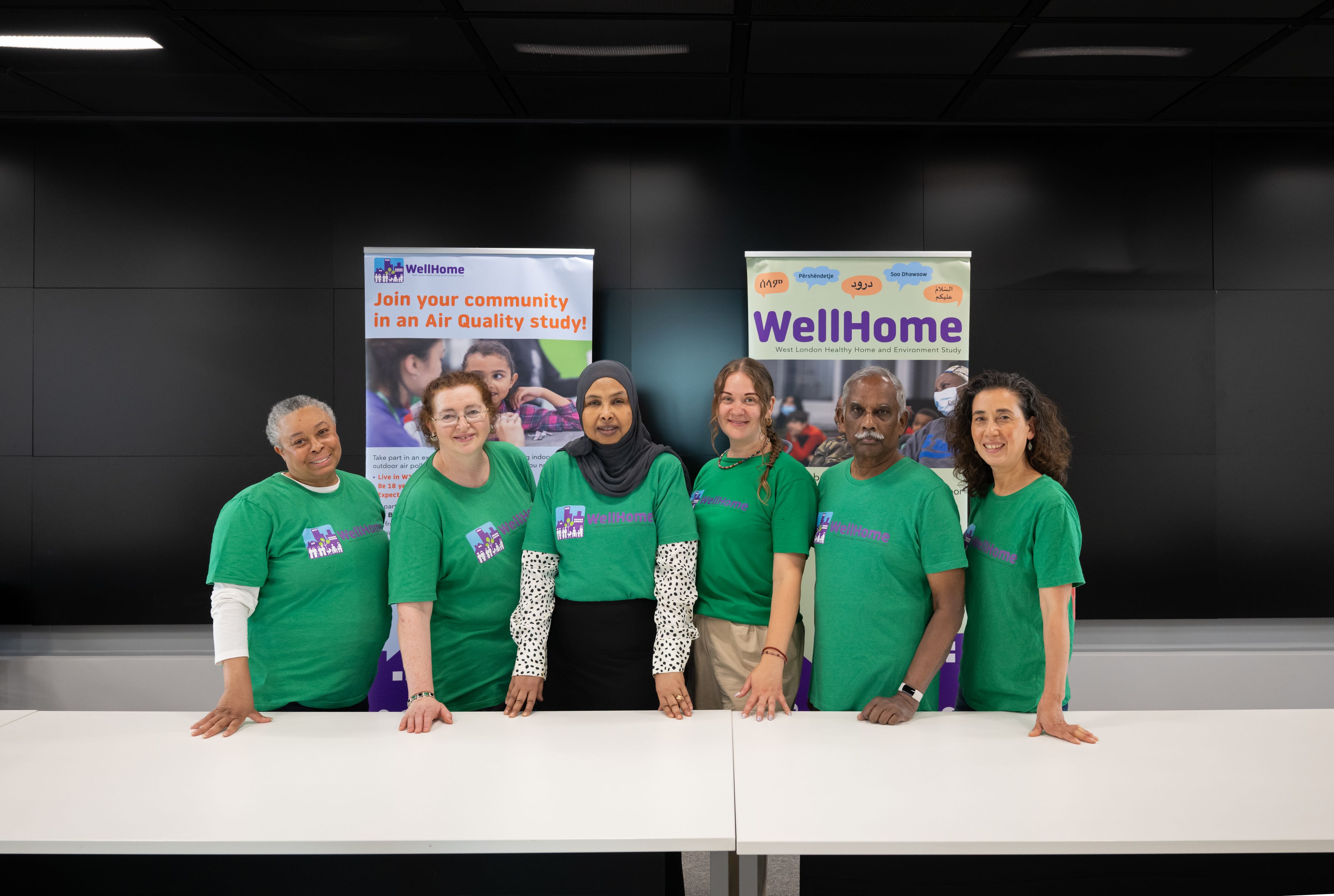 The group of Ambassadors smiling in a line in front of two WellHome Project vertical banners.