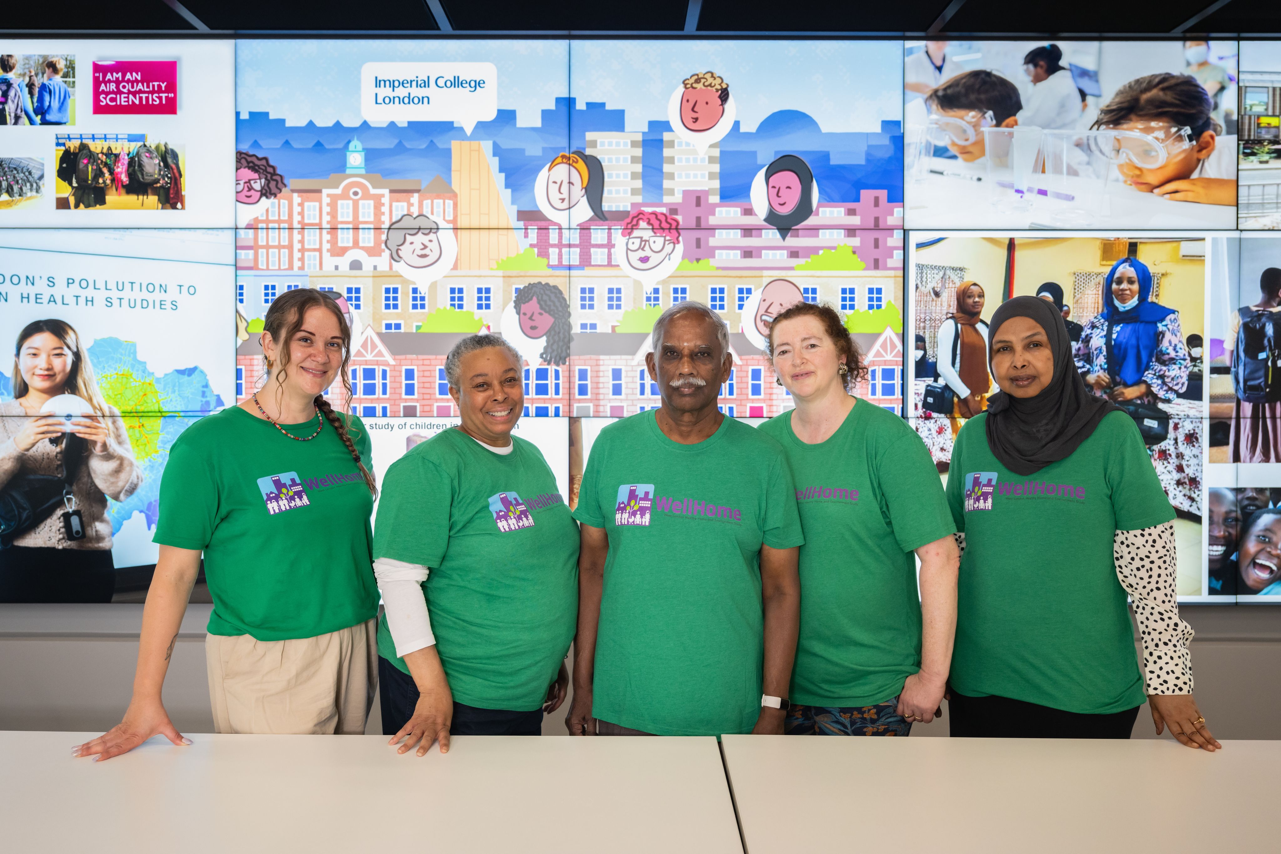 The Group of Ambassadors smiling in front of a large screen which is displaying a WellHome graphic.